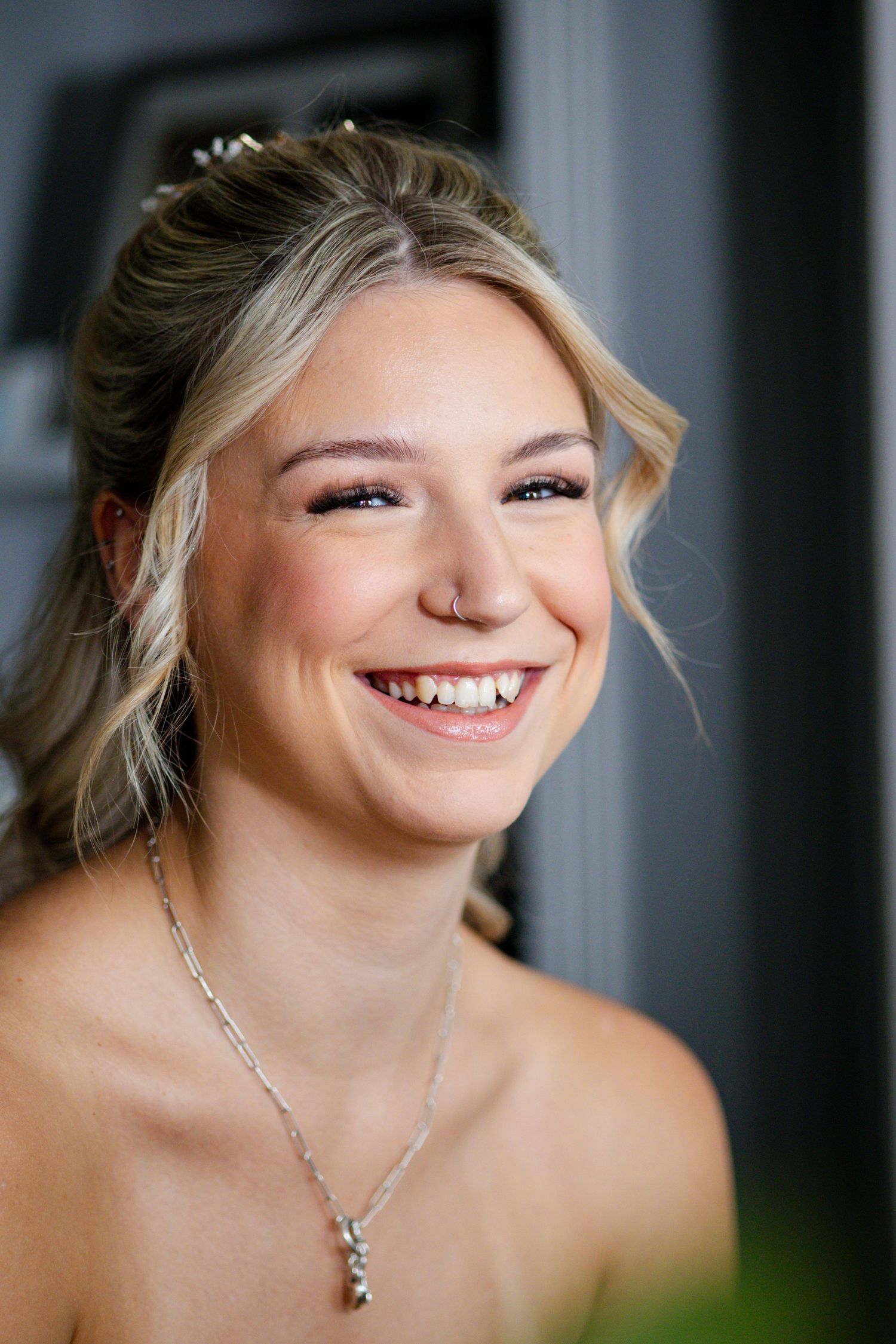Joyful blonde bride laughing with hair accessories and silver necklace on wedding day.