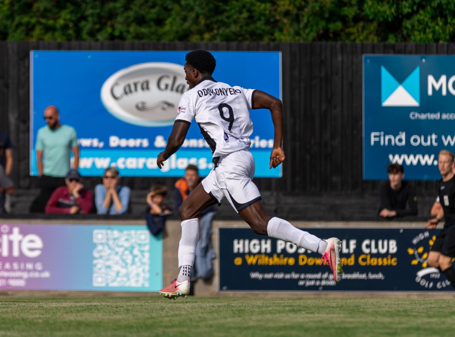 Soccer player wearing number 9 white jersey dribbles ball during a match at a grass field stadium.