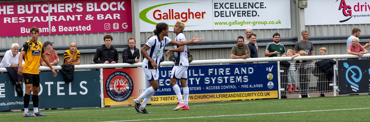 Soccer players compete on a grass pitch near advertising boards for Gallagher and The Butcher's Block restaurant.