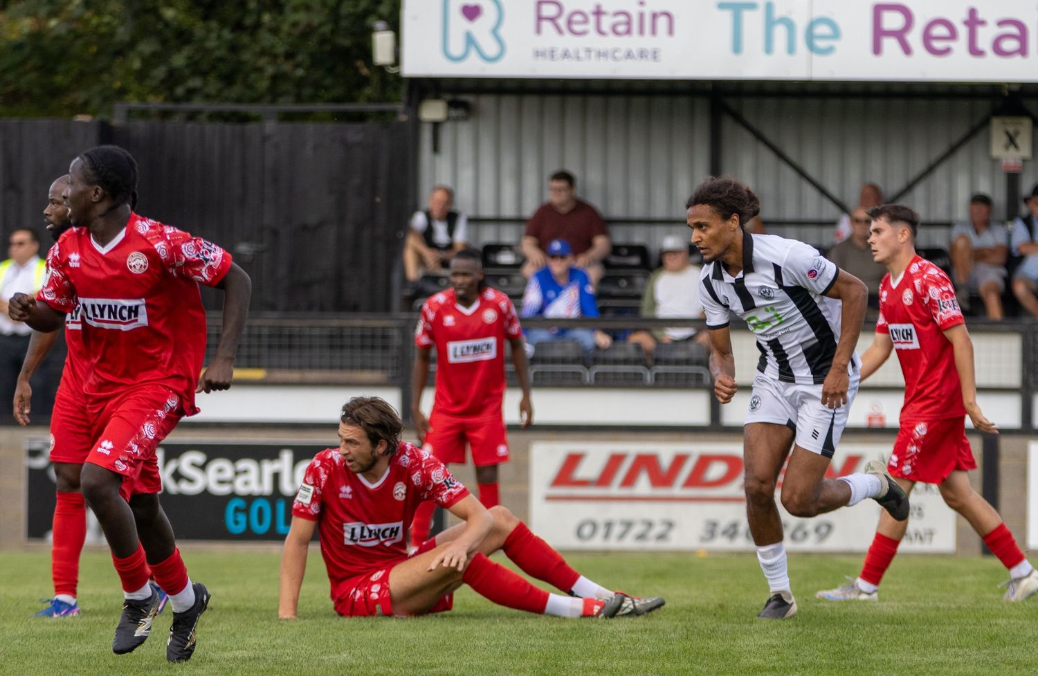 Football players in red and white kits compete during a match, with one player on the ground near advertising boards.