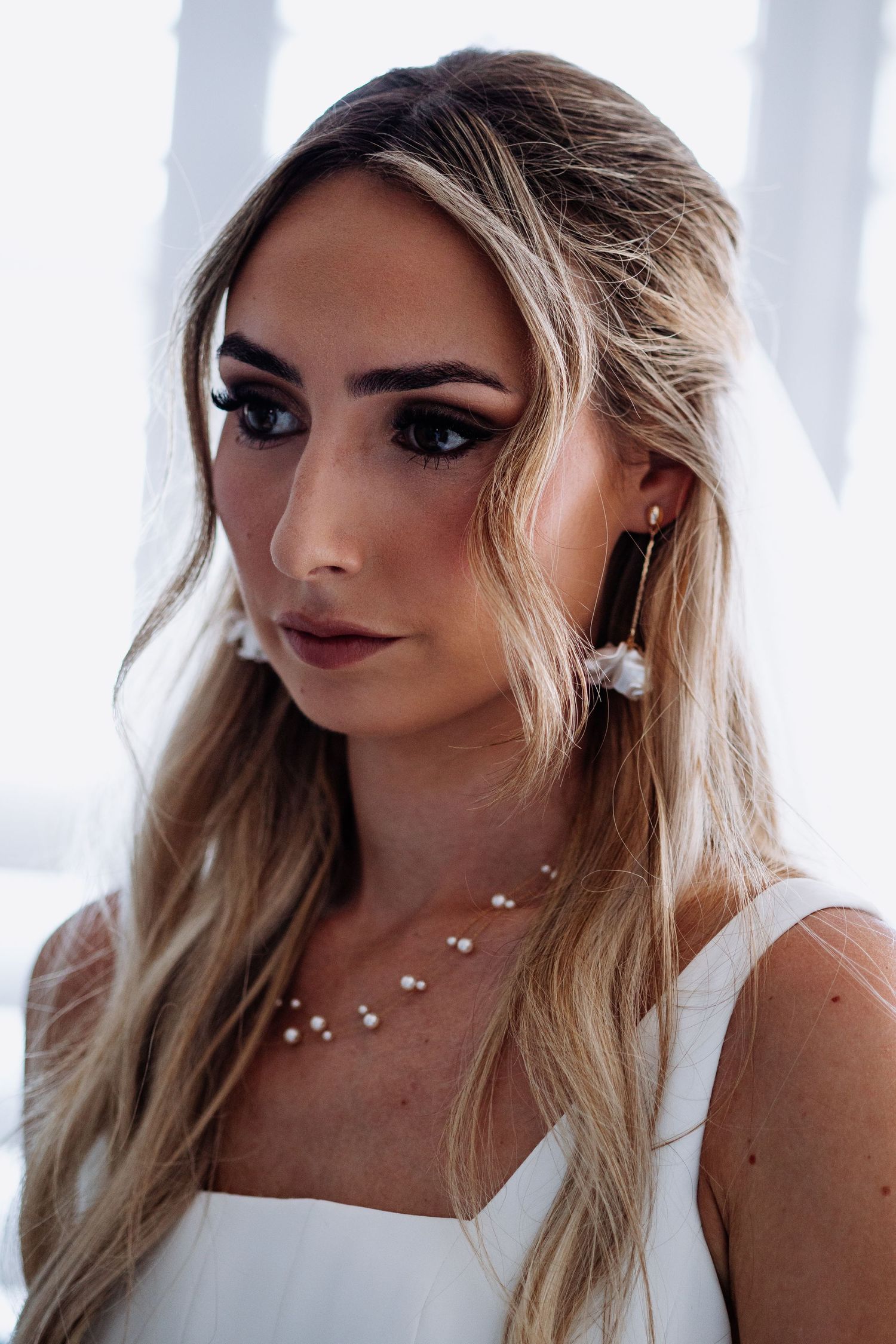 Beautiful bride with smoky eye makeup wearing pearl necklace and gold drop earrings with veil.