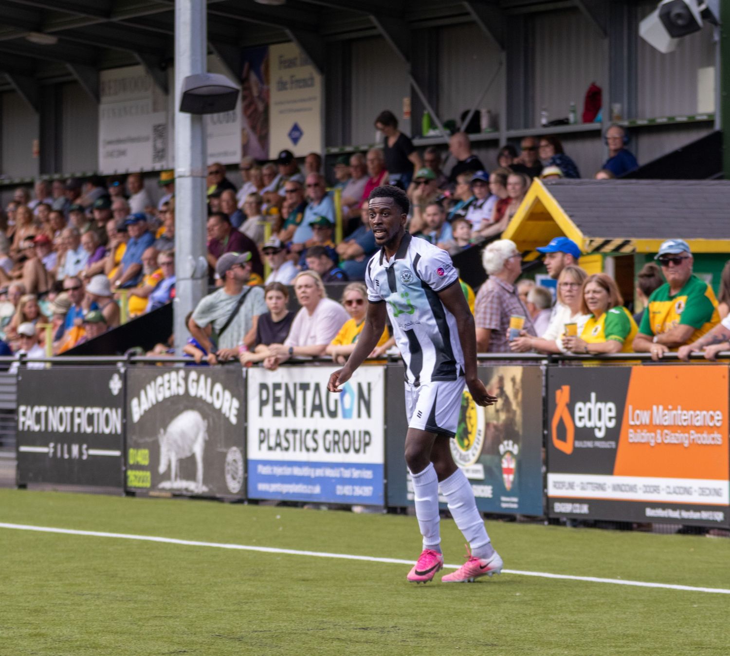 A Black footballer in white and black kit gestures on the pitch during a non-league football match.