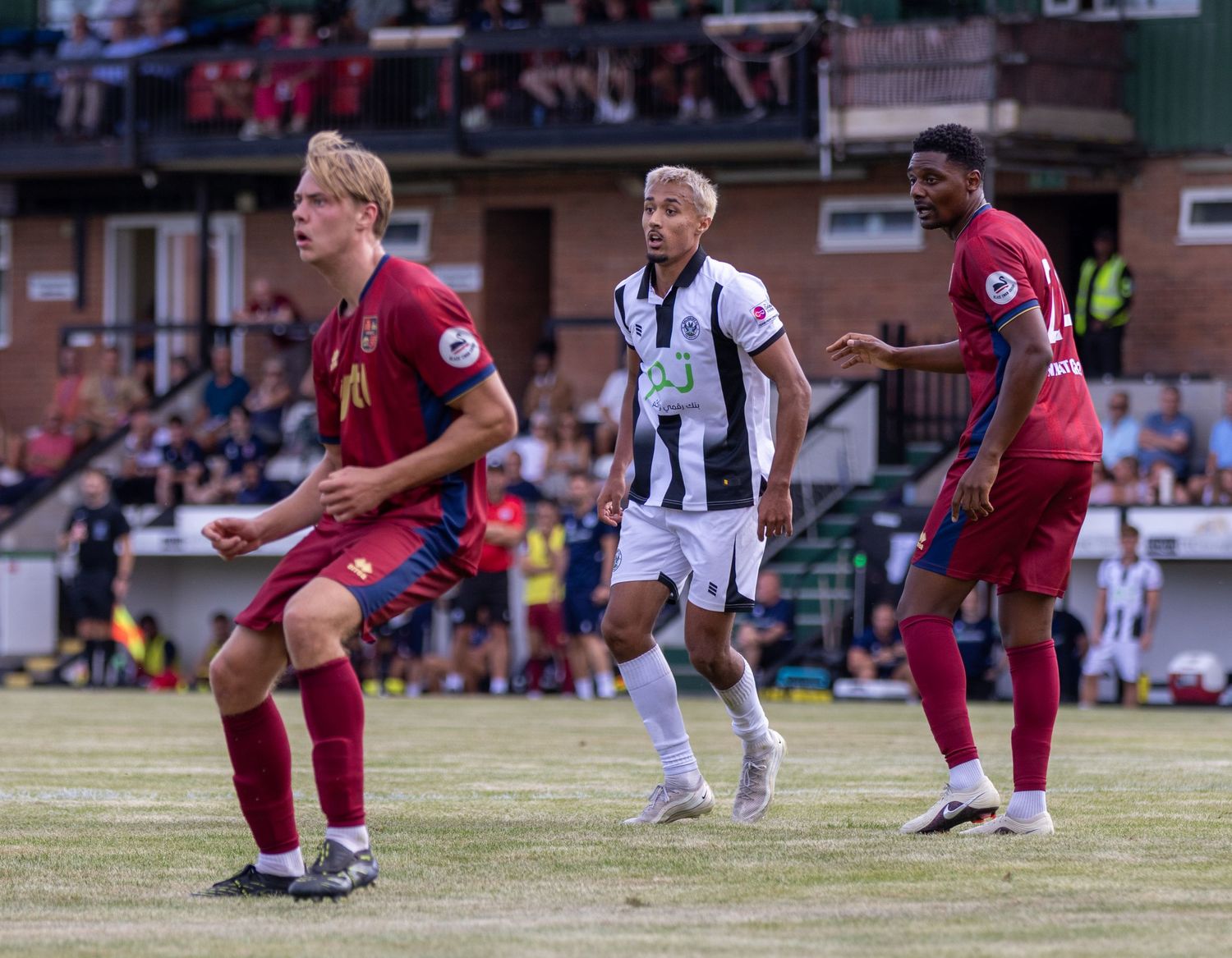 Players in claret and black-and-white kits contest possession during a sunny outdoor football match.