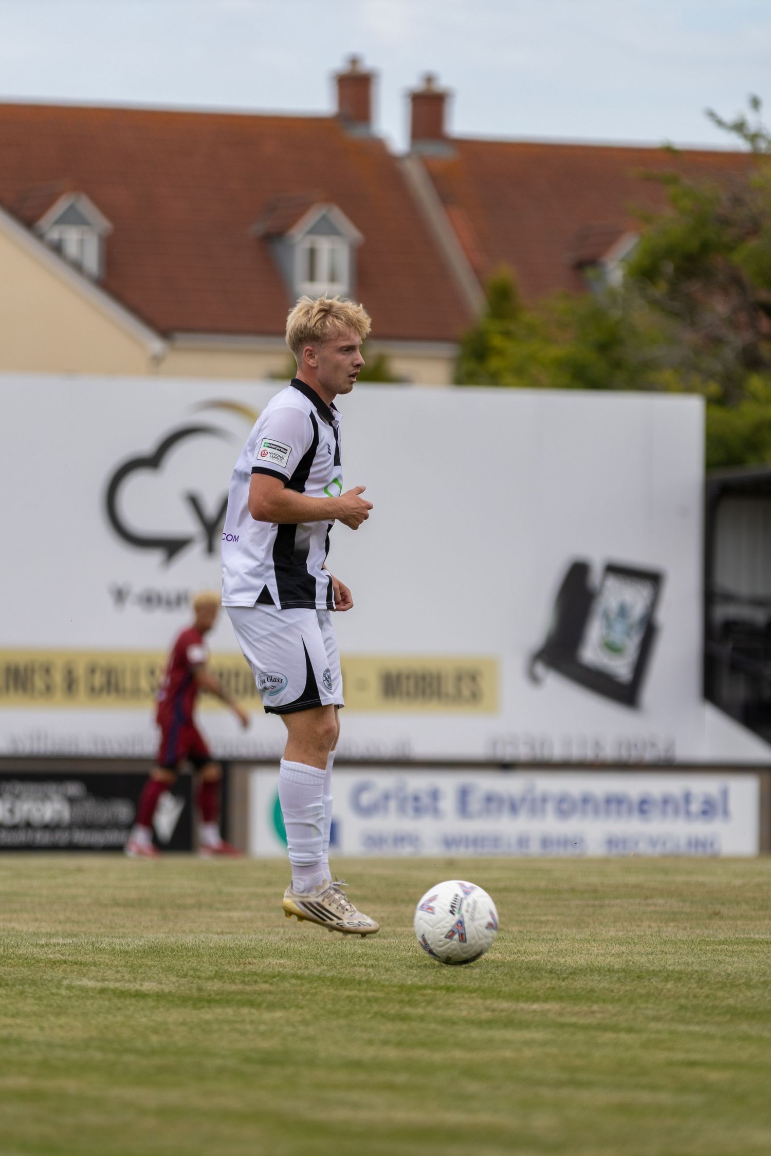 Blonde footballer in black and white striped kit controls ball during outdoor match daytime.