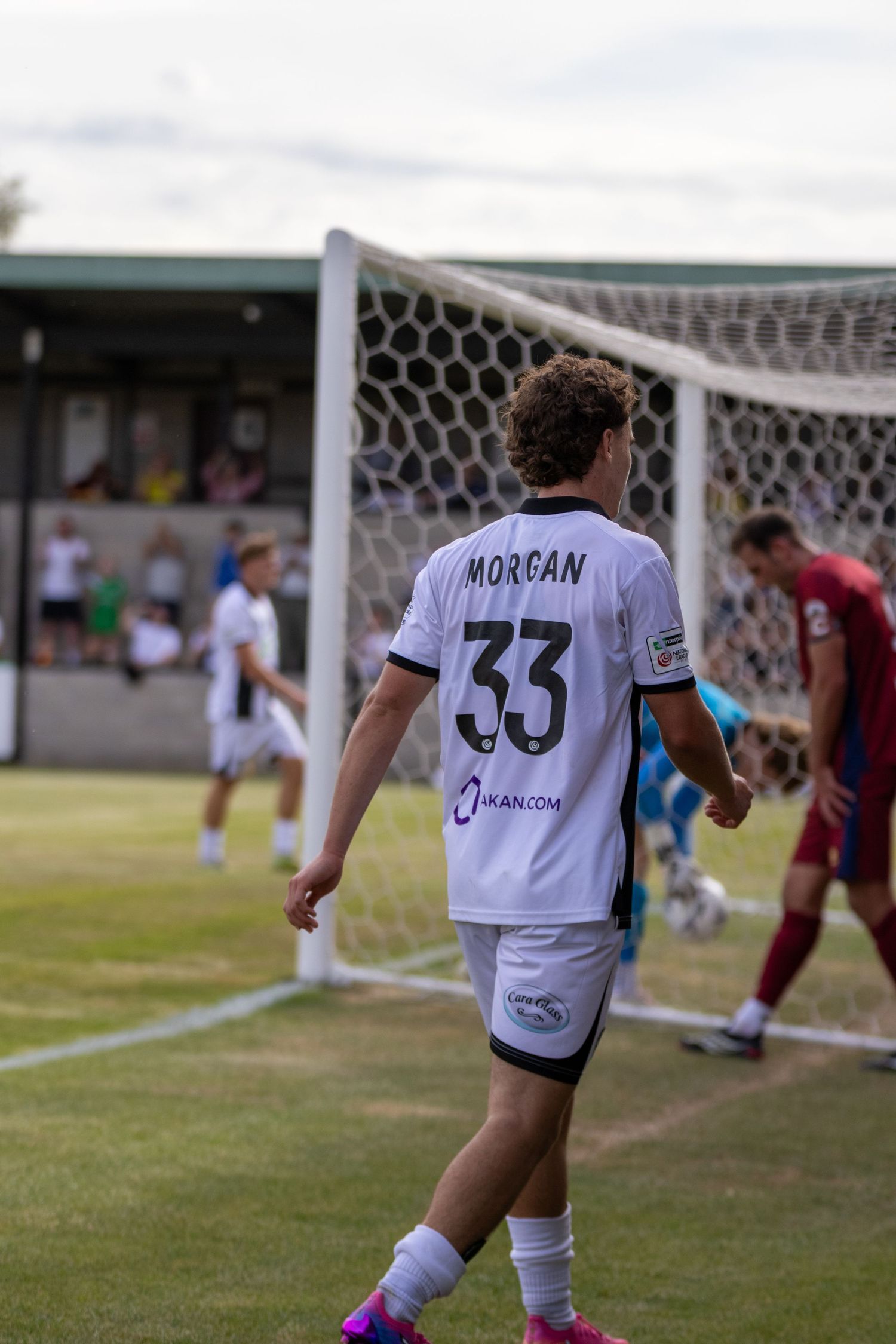 Player MORGAN number 33 in white away kit walks near goalpost during non-league football match.