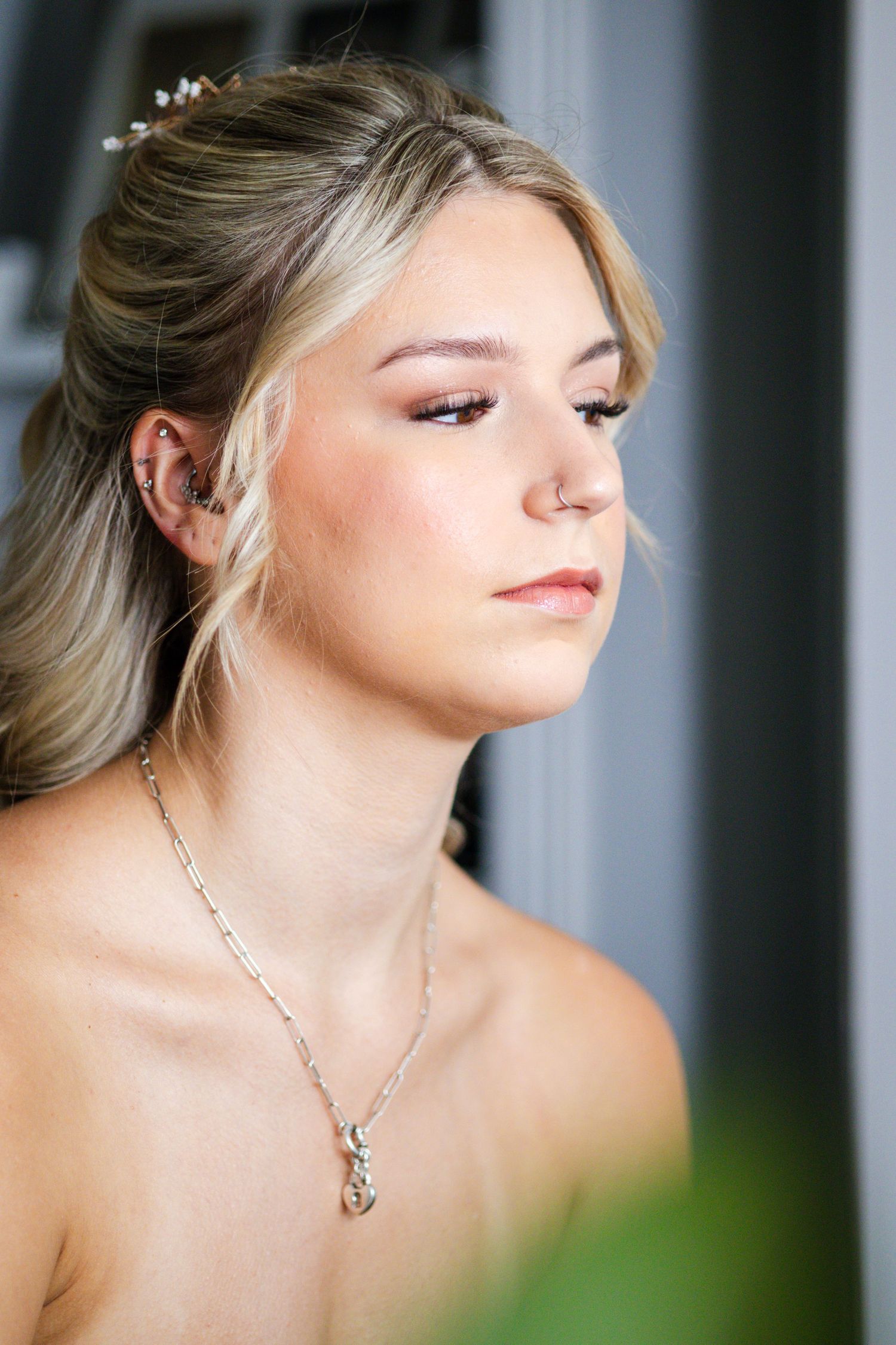 Elegant bride with hair accessories and silver necklace gazing downward before wedding.
