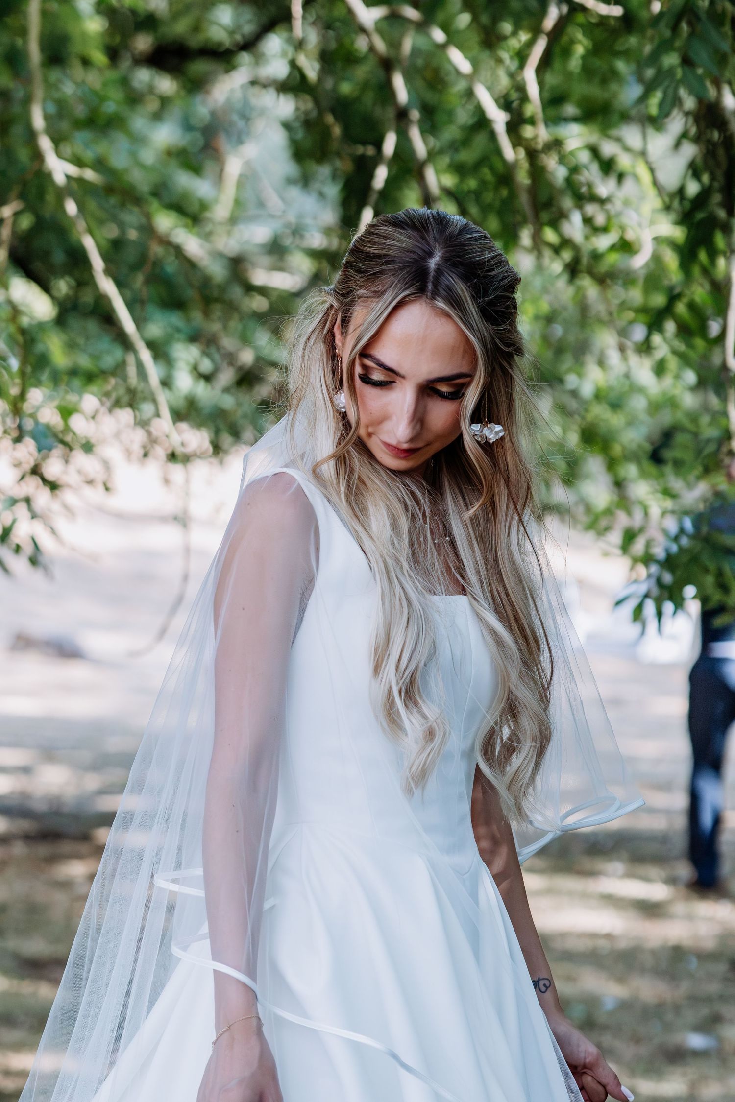 Beautiful bride with long blonde hair in white wedding dress and veil in a garden setting.
