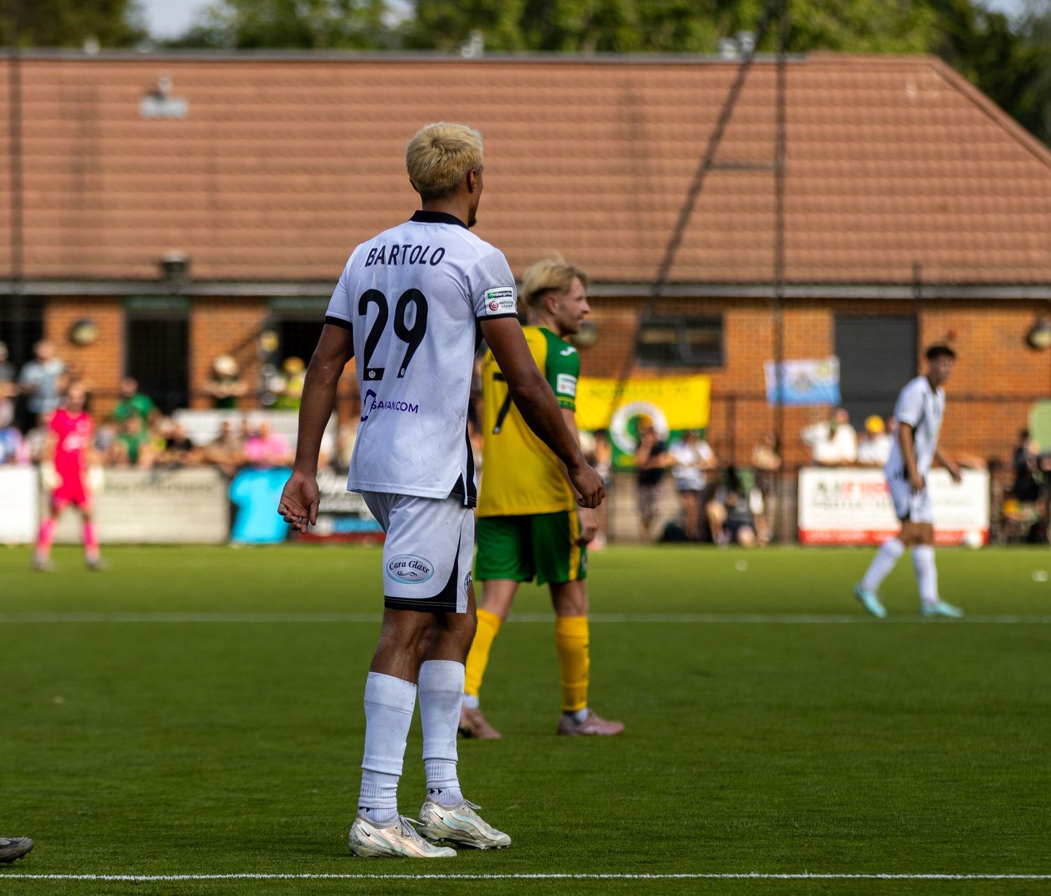 Bartolo number 29 in white away kit stands on green pitch during a sunny football match.