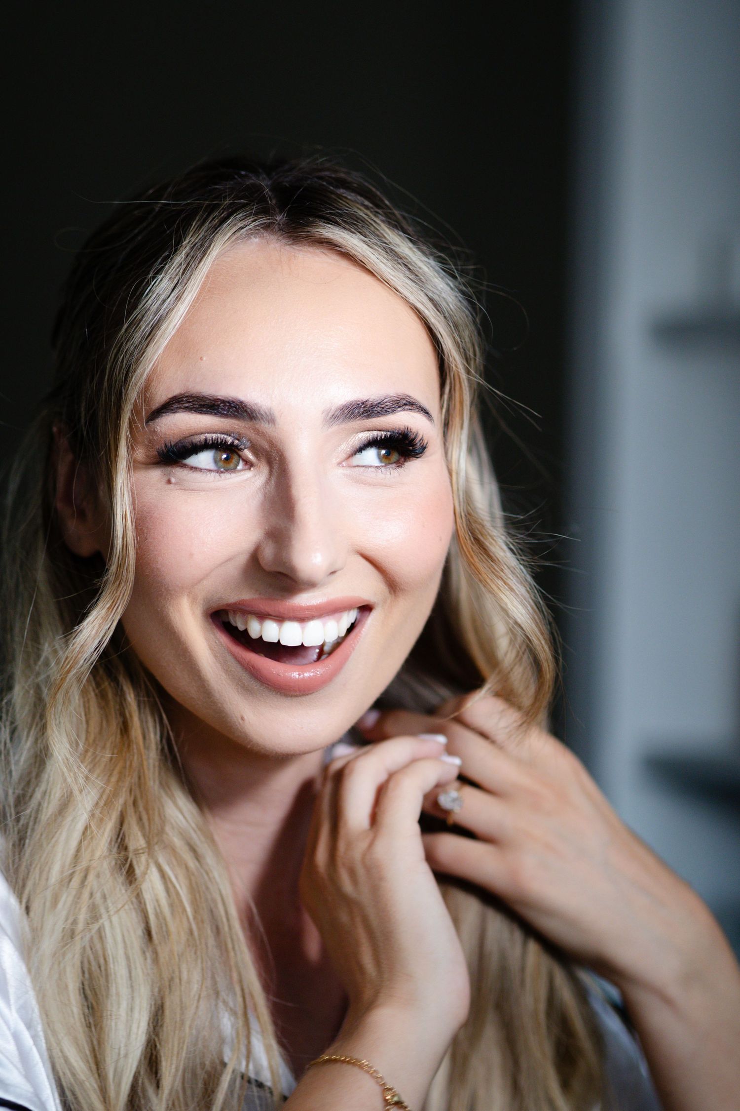 Happy blonde woman with bridal makeup laughing and looking up while wearing a white satin robe.