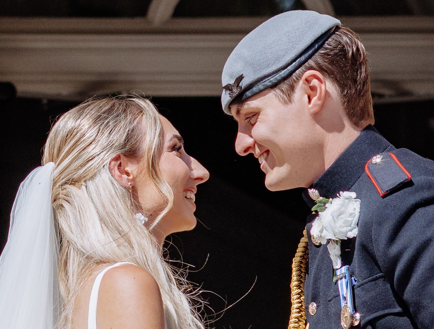 Close-up of smiling bride in veil and groom in military cap gazing at each other on wedding day.