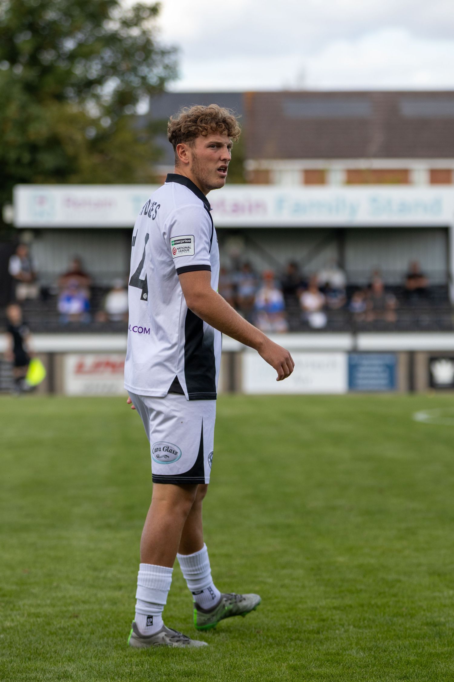 Young football player in white kit with number 4 jersey on green pitch during a match at a non-league ground.