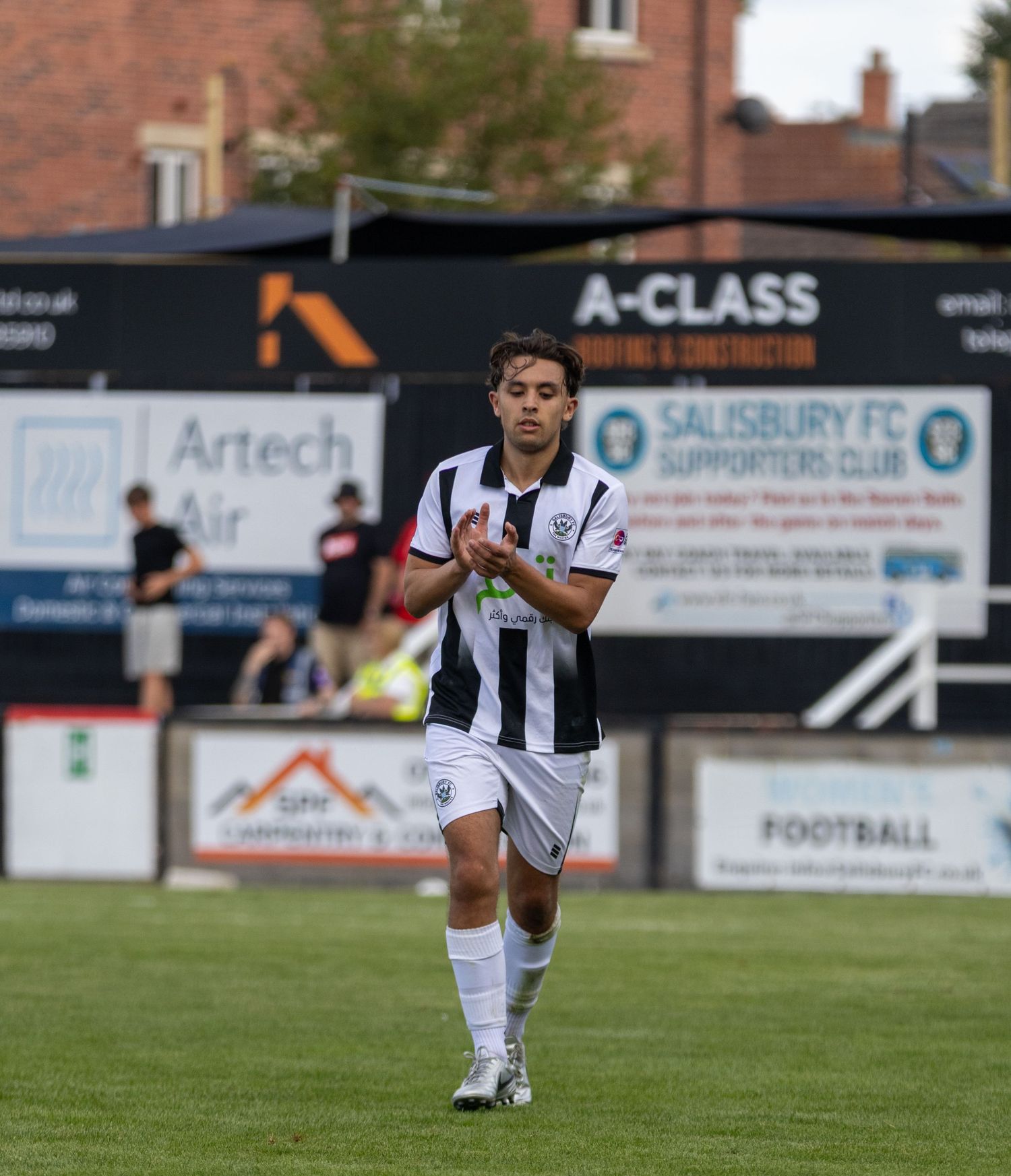 Soccer player in black and white kit walks on pitch at Salisbury FC ground during a match.