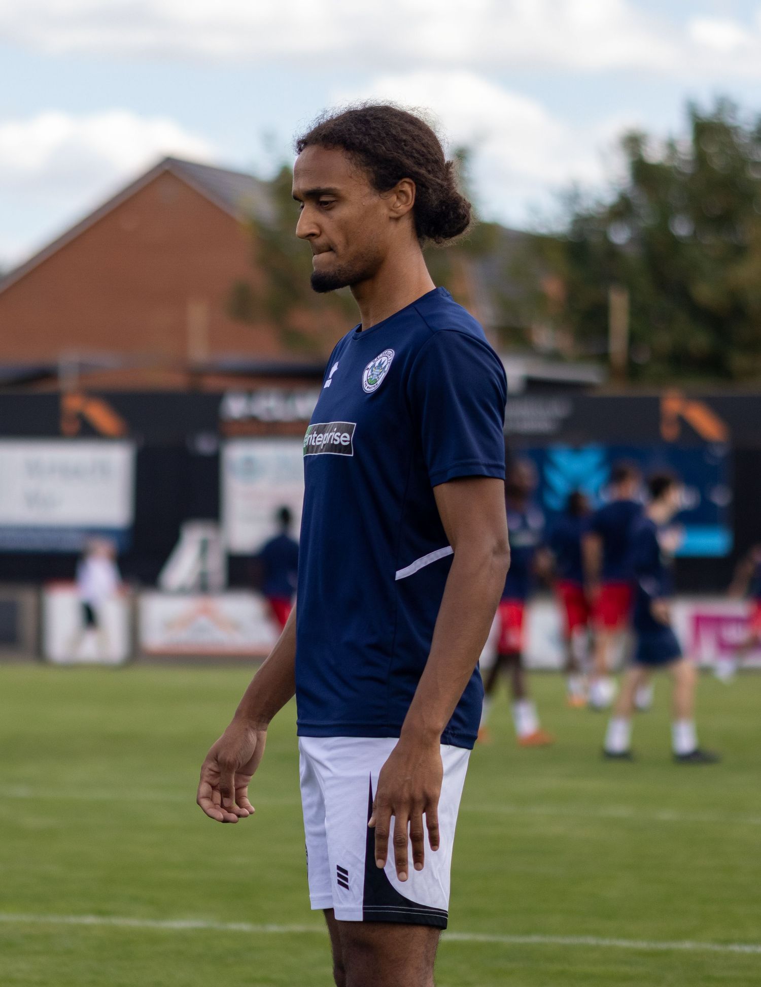 A young football player in navy blue kit stands on a grass pitch during a soccer match warm-up.
