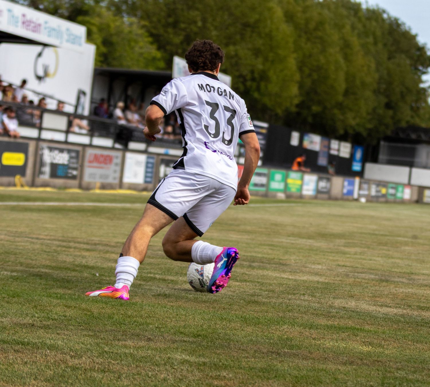 Soccer player MORGAN number 33 in white kit controls ball on grass pitch during match.