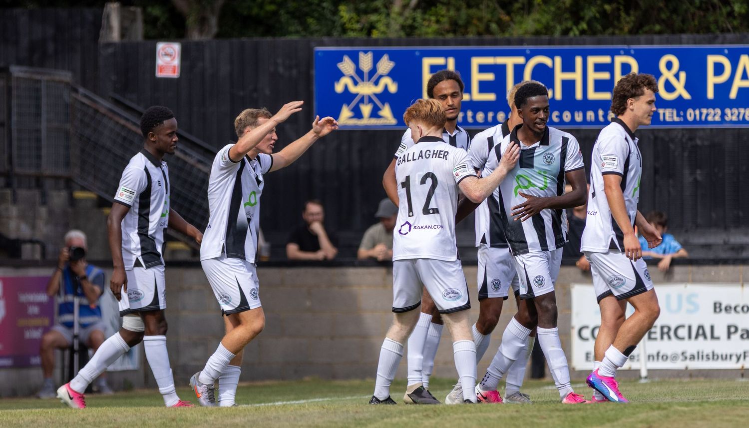 Salisbury FC players in black and white celebrate a goal together in front of Fletcher & Partners signage.