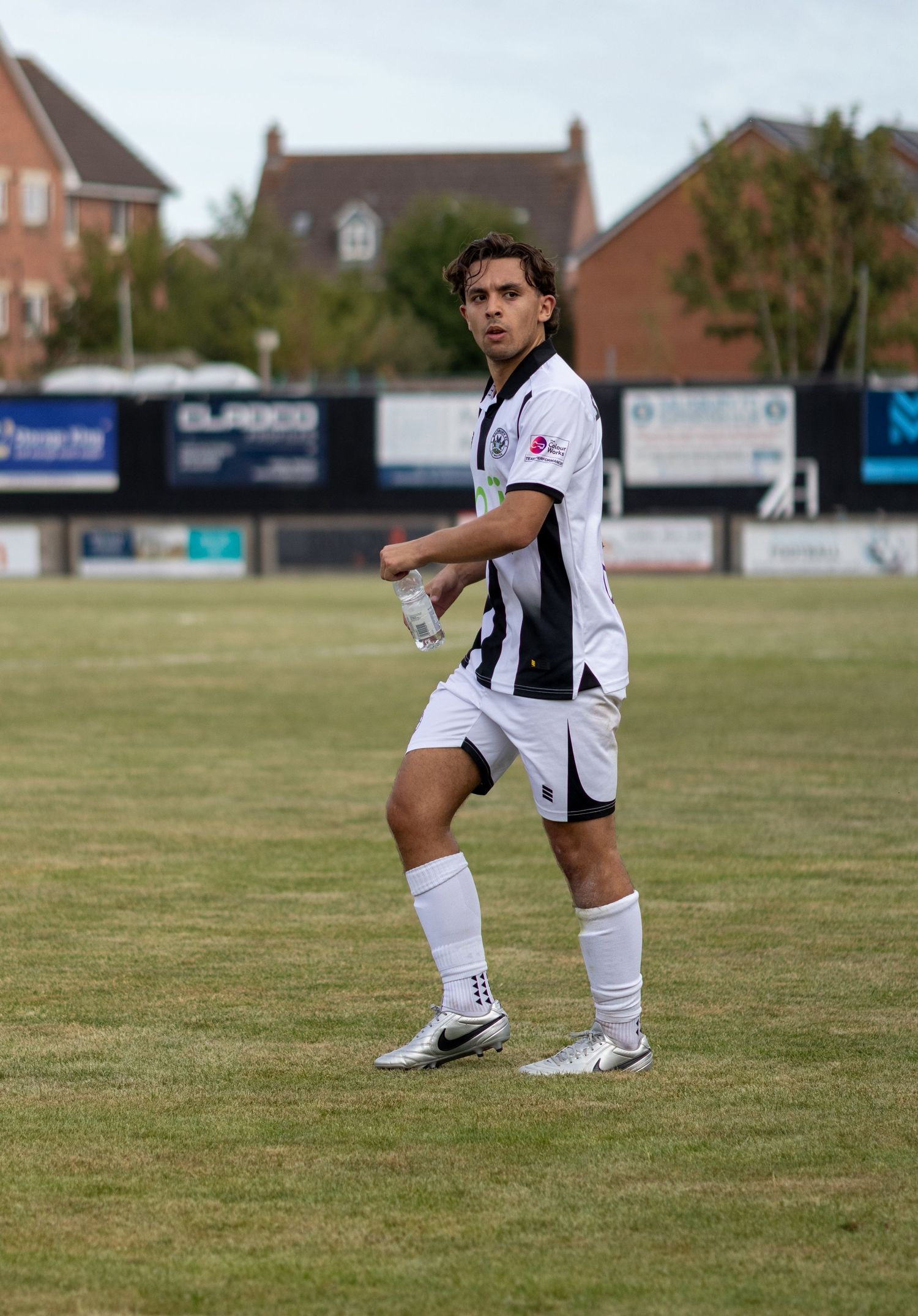 A male soccer player in a white and black kit walks on a grass field during a match.