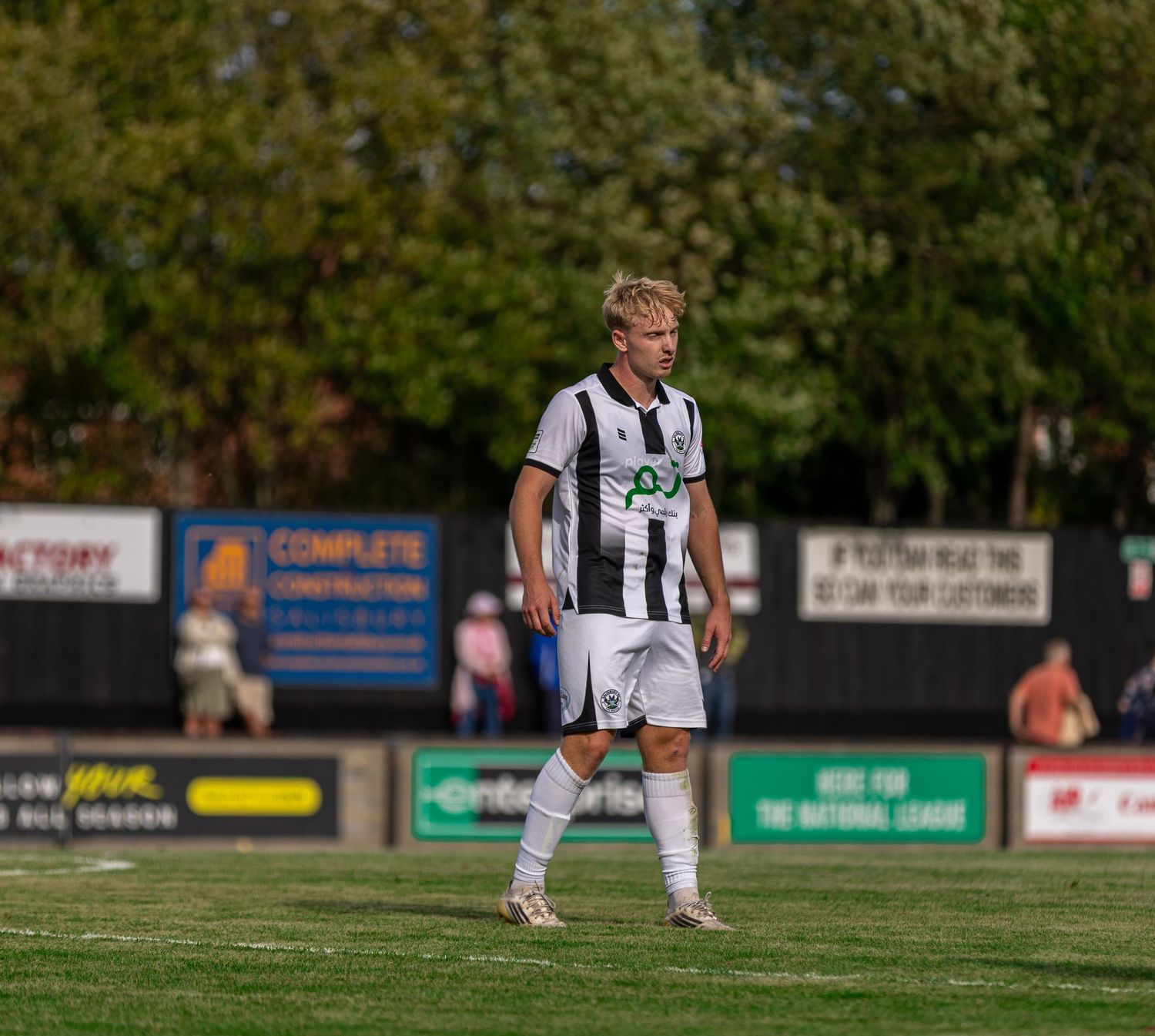 Young male soccer player in black and white uniform walking on green field during a sunny outdoor match.
