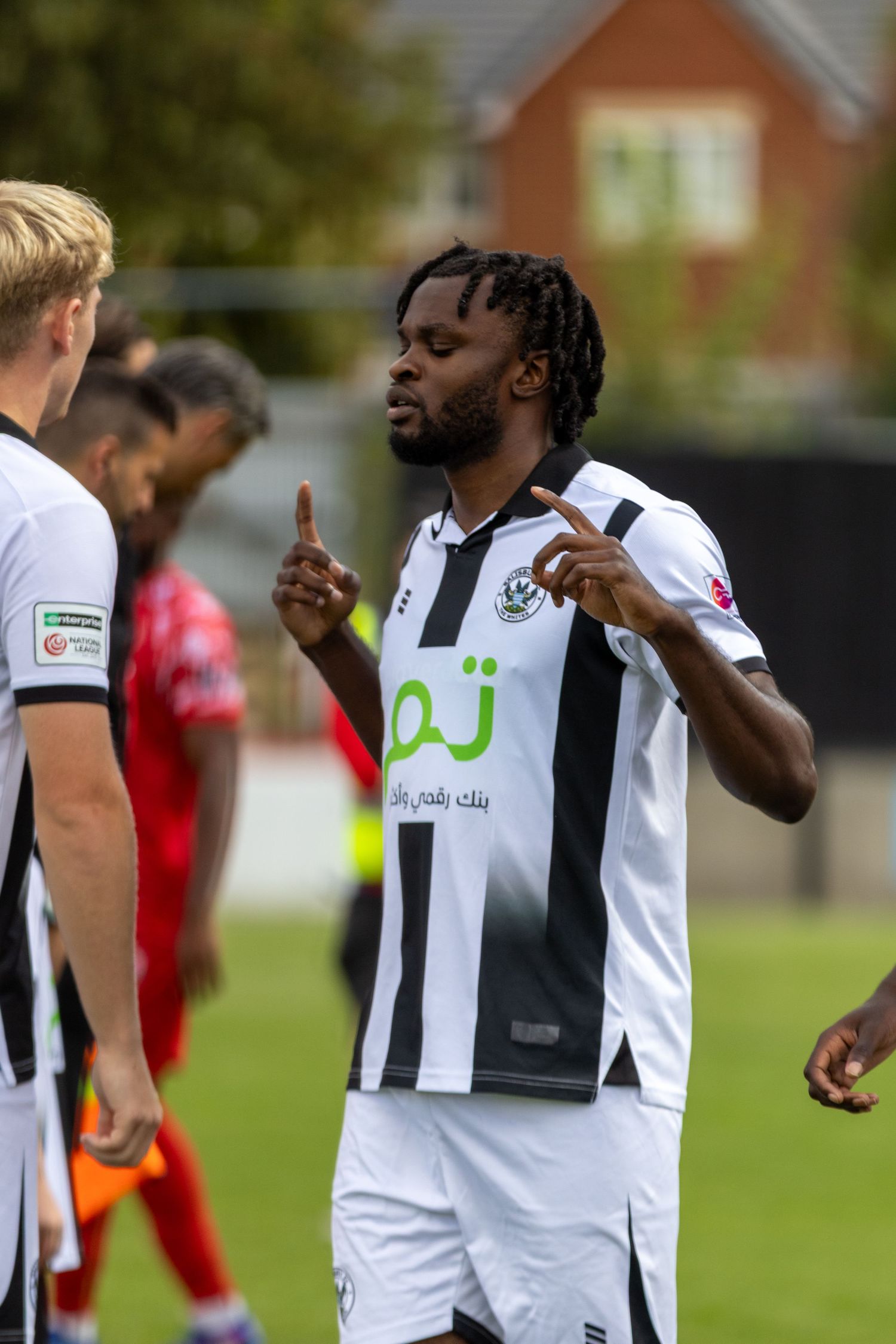 A footballer in a black and white striped kit signals with his fingers on the pitch.