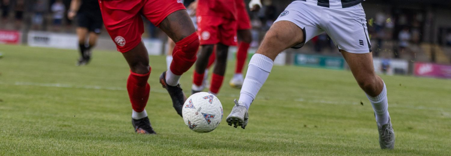 Two soccer players compete for the ball during a match on a green grass field.