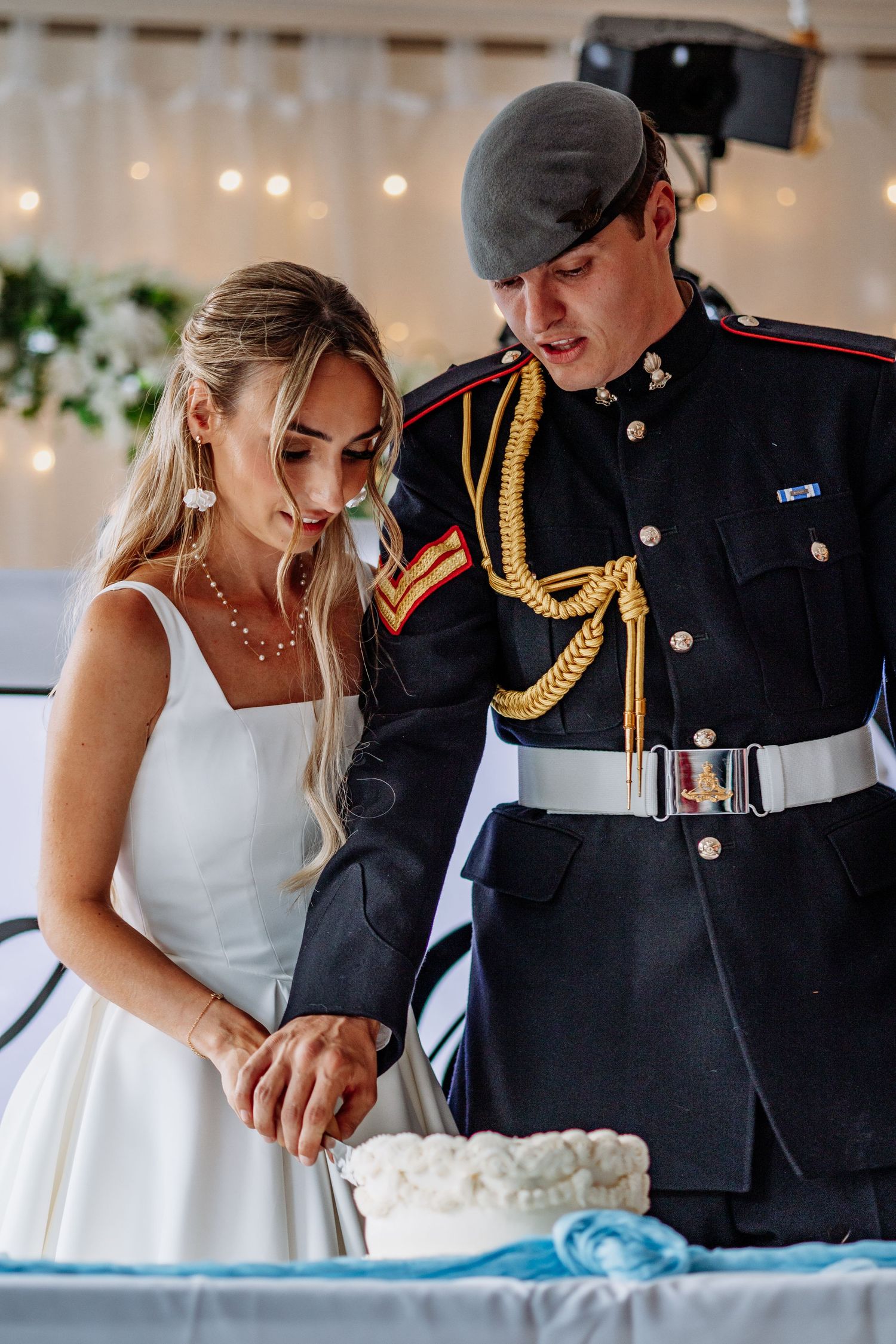 Newlyweds cutting white wedding cake, groom wearing military dress uniform with gold braiding.