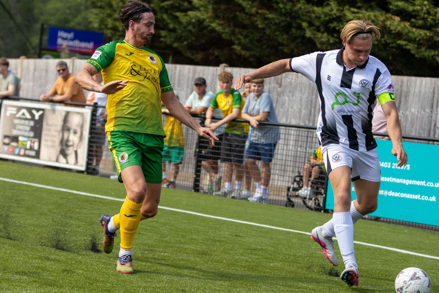 Two football players compete for the ball, one in yellow-green and one in white-black kit outdoors.