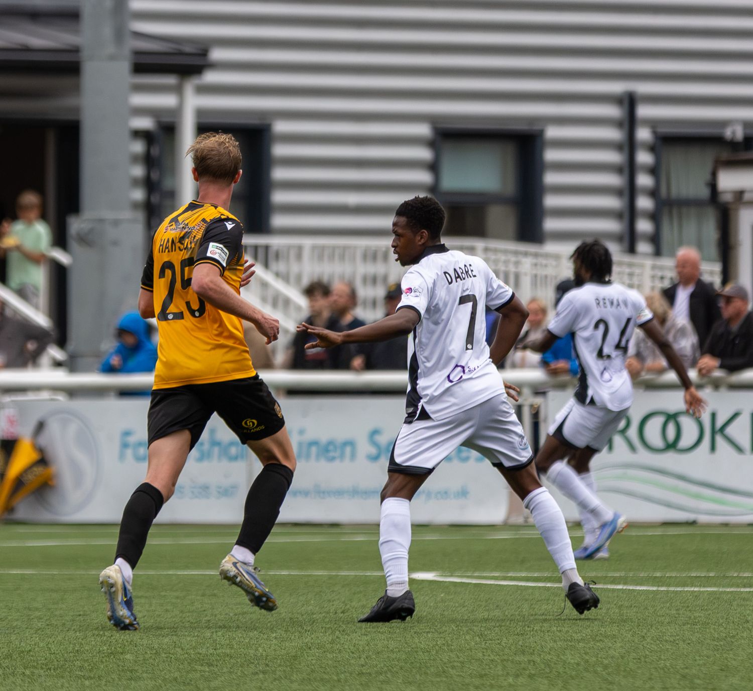Soccer players in action during a match, player number 7 in white kit competing against number 23 in yellow.