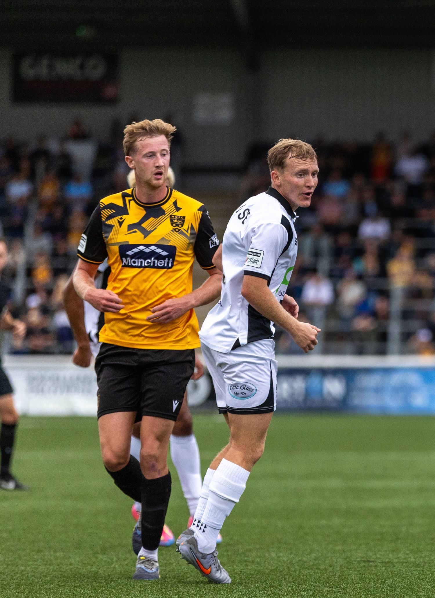 Two soccer players competing on a green field, one in yellow and one in white uniform, during a match.