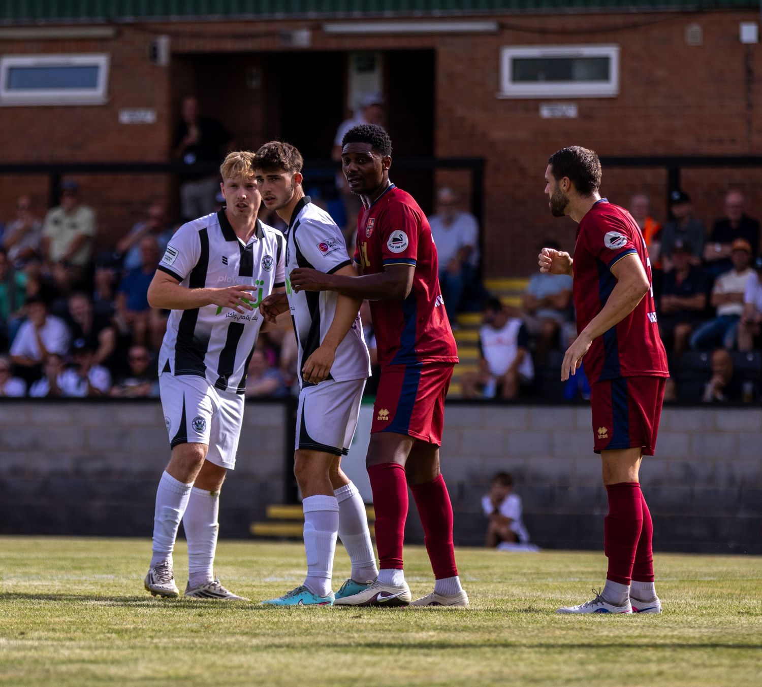 Football players in black-white and red kits engage in a tense confrontation during a non-league match.