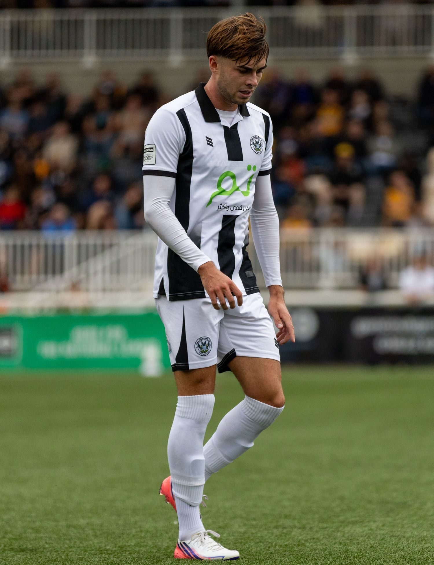 Soccer player in black and white striped kit walking on the pitch during a match.