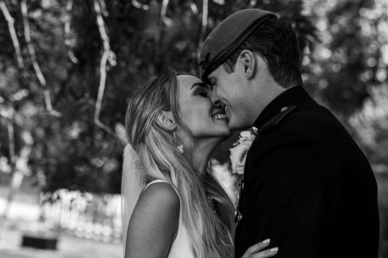 Black and white photo of bride and groom sharing a joyful wedding kiss.