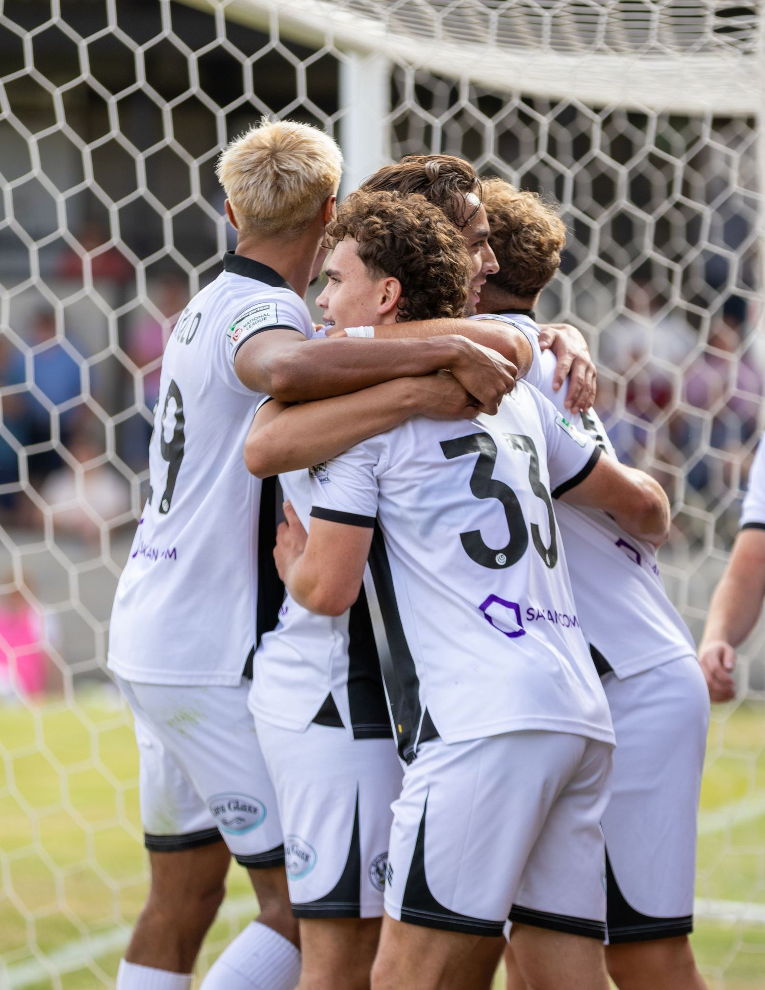 Soccer players in white uniforms celebrate together near the goal net during a match.