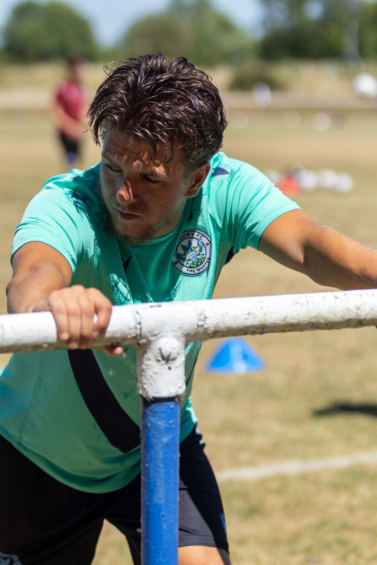 Focused footballer in teal kit performing bar push exercise during pre-season training.
