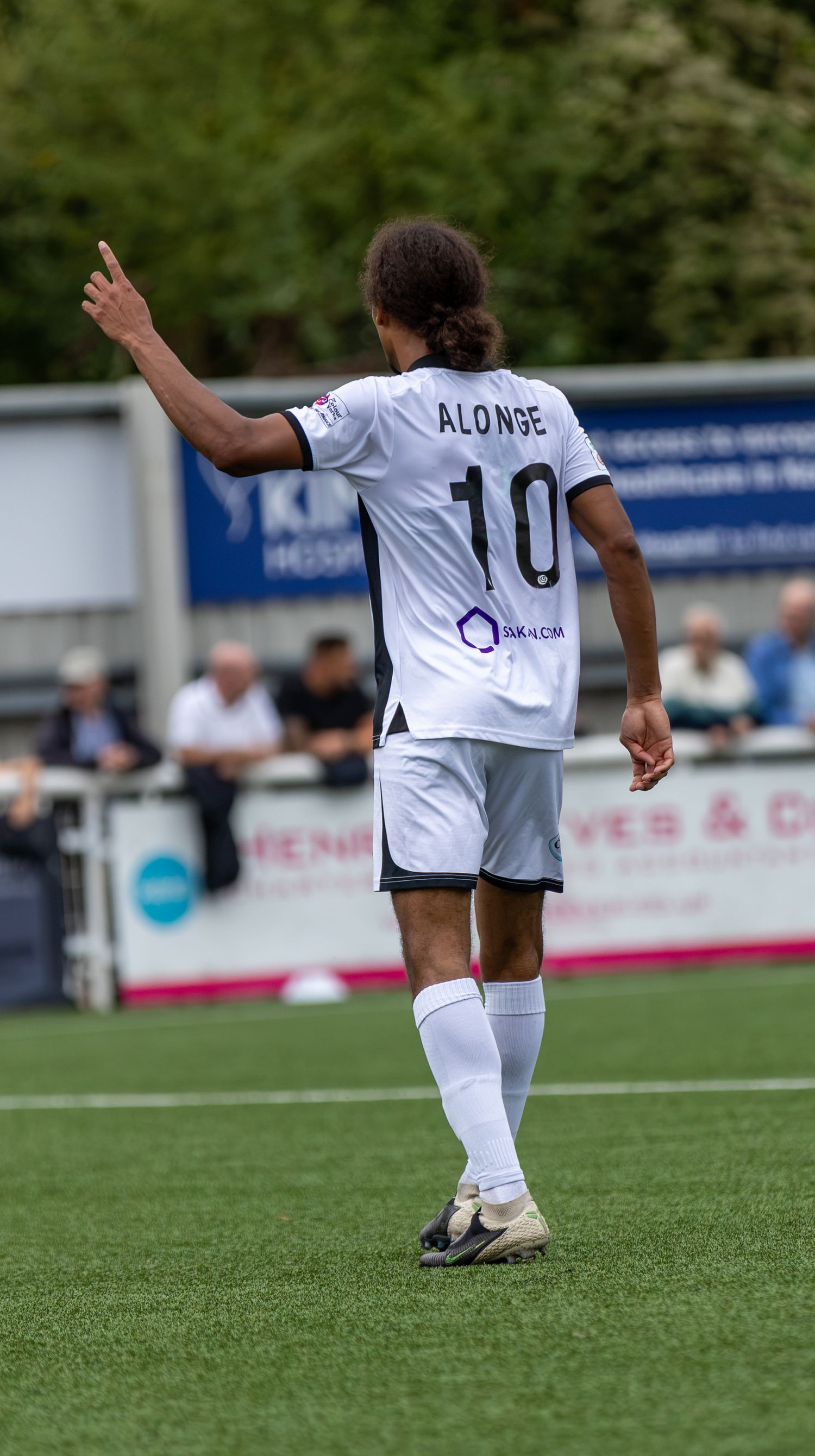 Soccer player Alonge wearing number 10 white jersey raises hand on green pitch during a match.