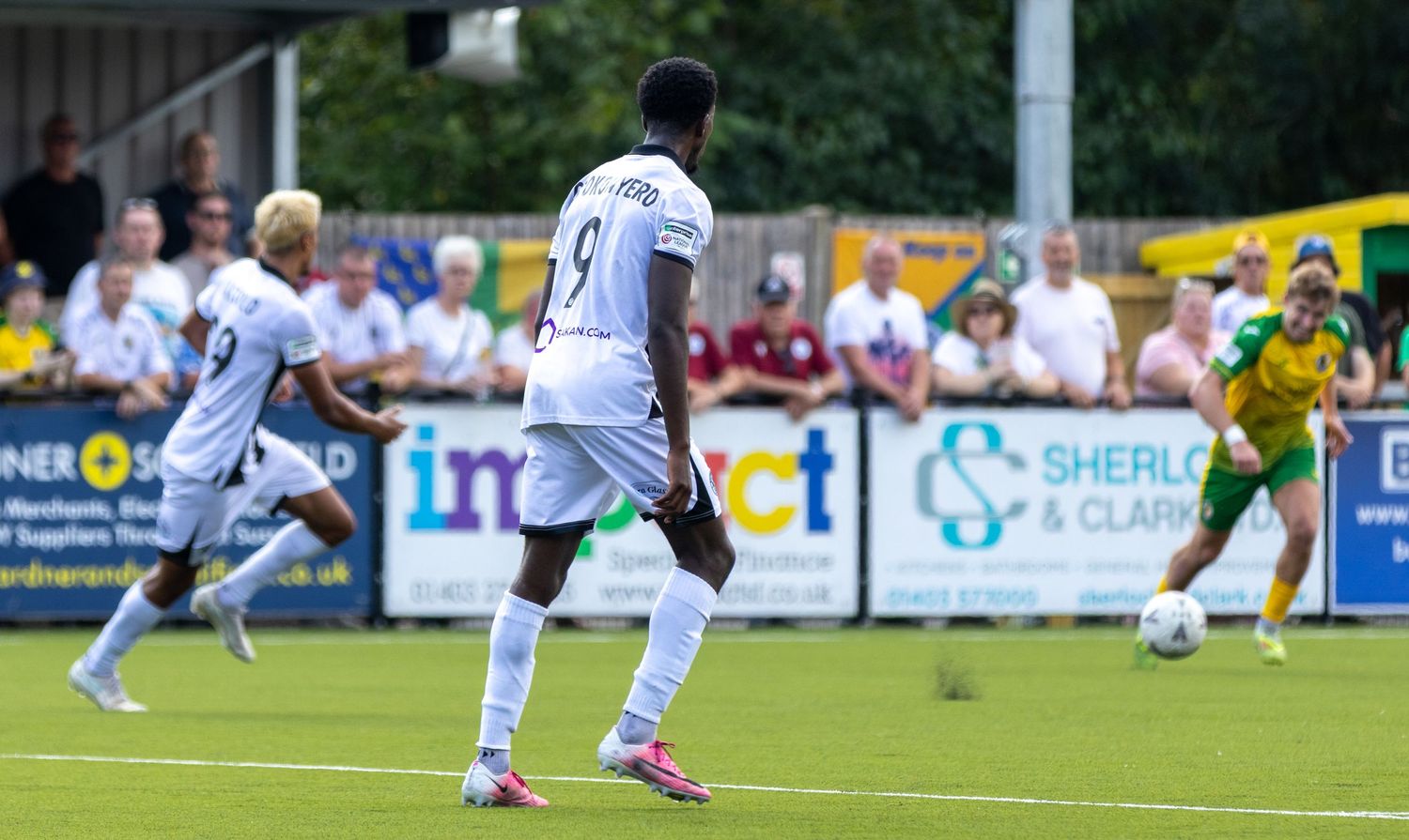 A footballer wearing number 9 white kit prepares to receive a pass during a sunny outdoor match.