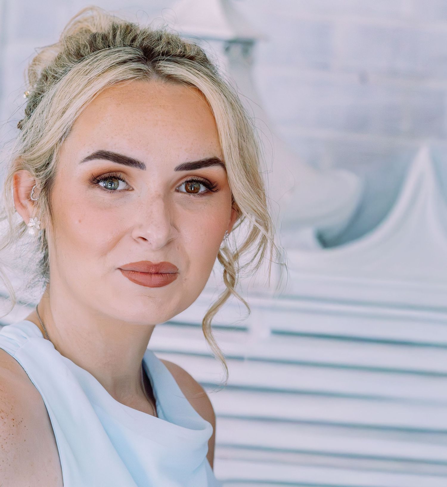 Close-up portrait of blonde bride with updo hairstyle wearing pearl earrings and white dress.