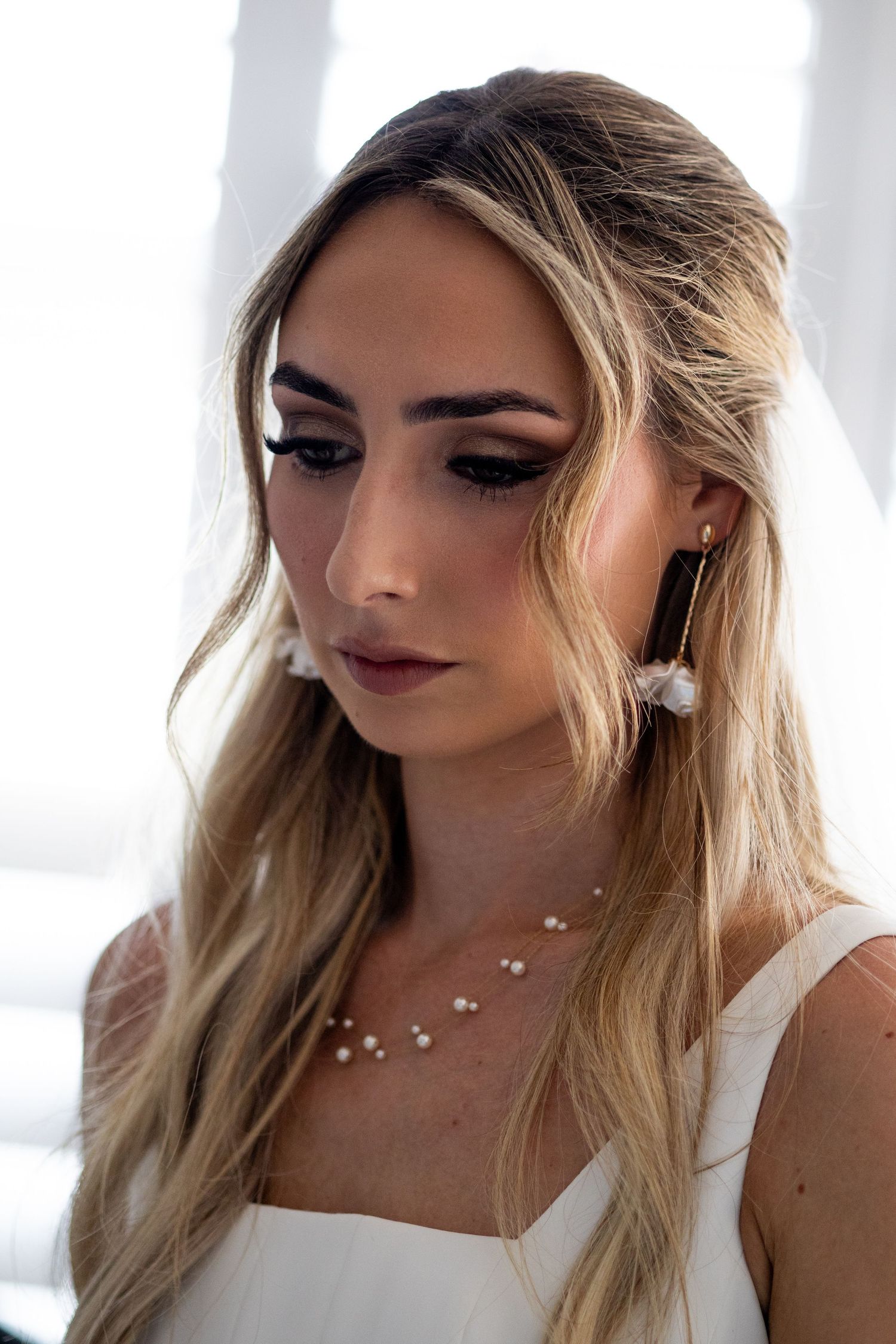 Close-up portrait of bride with smoky eye makeup wearing pearl necklace and statement drop earrings.