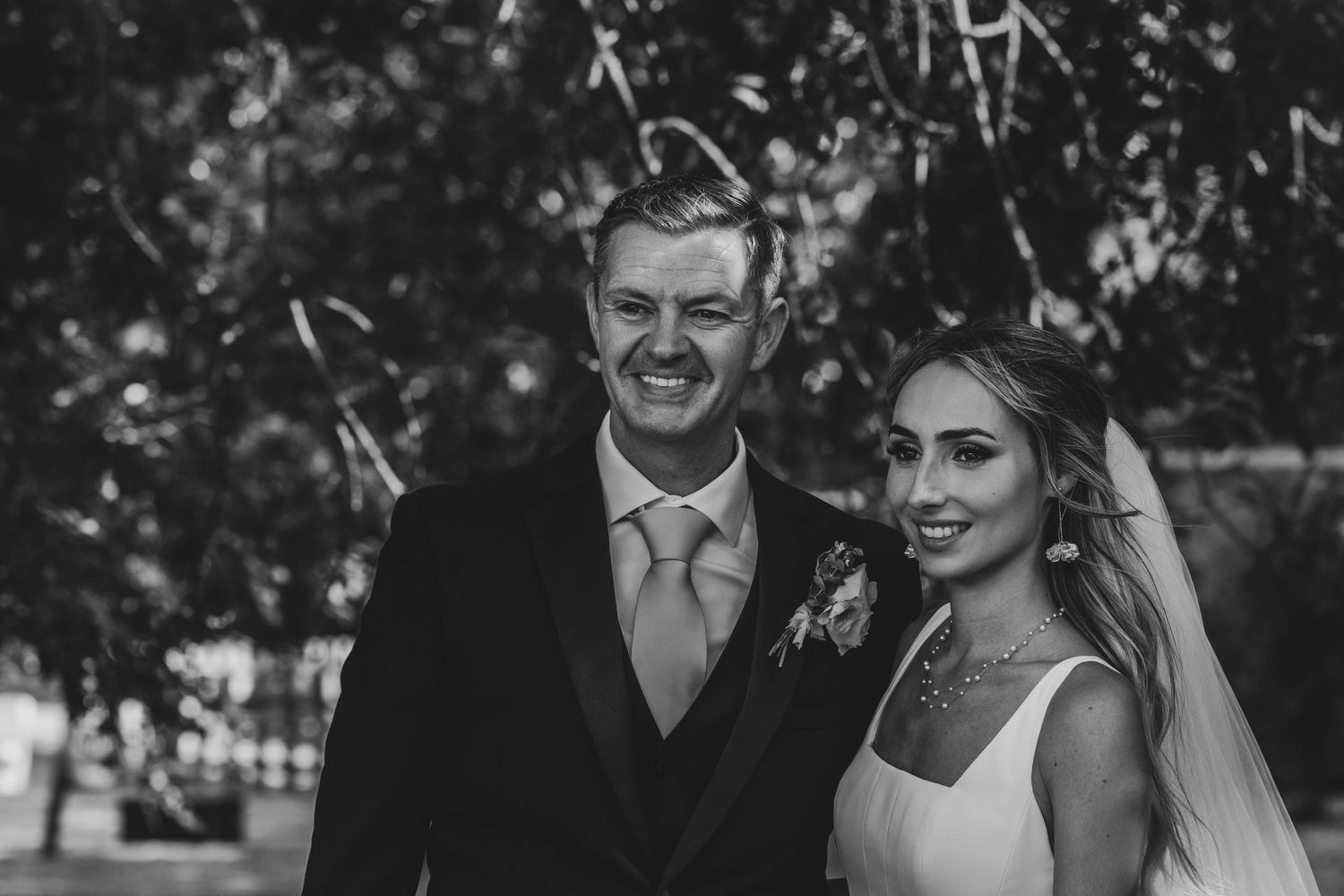 Black and white wedding portrait of smiling couple, groom in suit with boutonniere beside veiled bride.