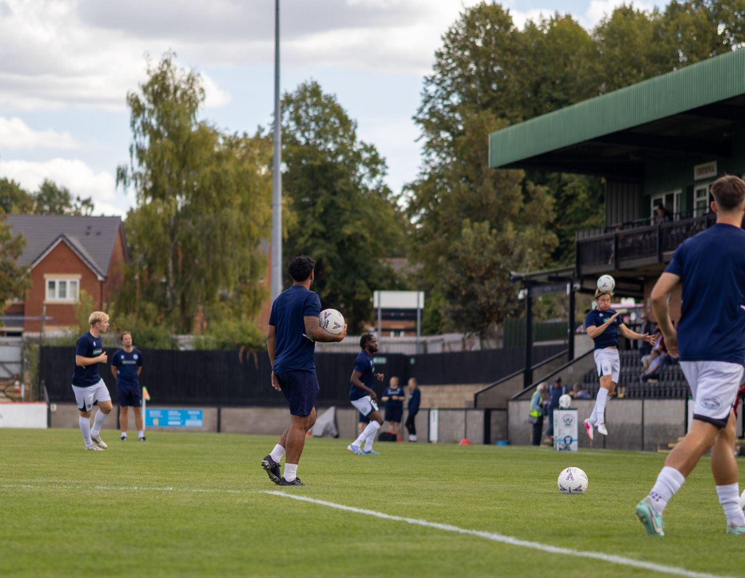 Football players in navy training kits warm up with passing drills on the pitch before a match.