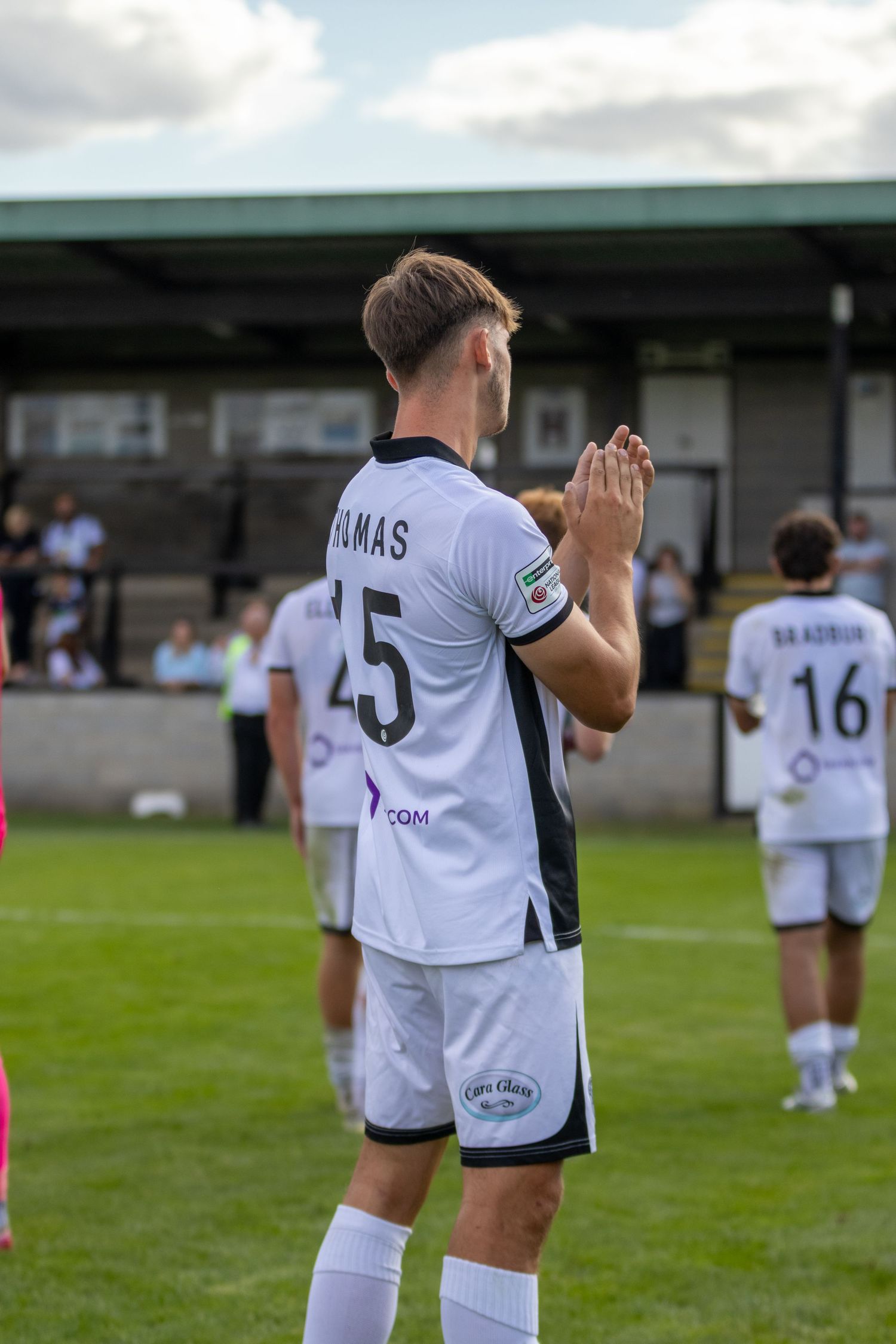 football player number 15 in white kit claps hands on green pitch during a football match.