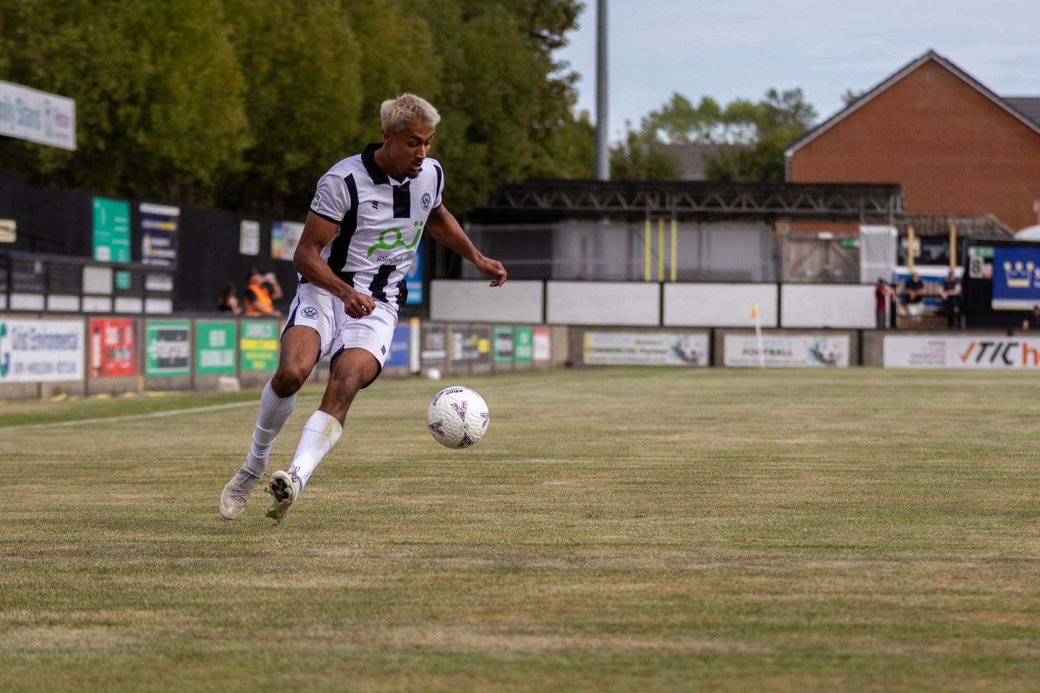 Soccer player in black and white kit prepares to kick ball on green pitch during sunny outdoor match.