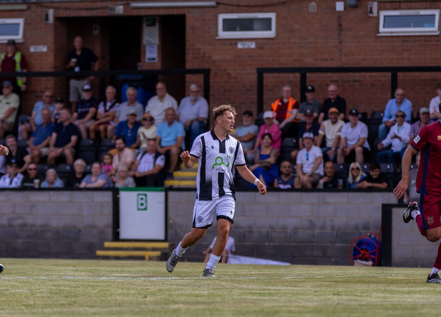 A young soccer player in black and white celebrates on the pitch with spectators watching in the stands.