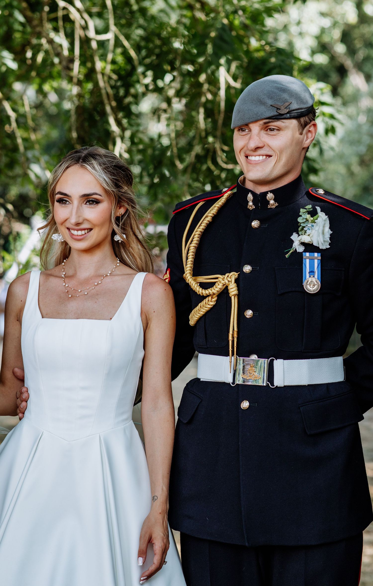 Bride in white gown standing with groom in formal military dress uniform with medals outdoors.