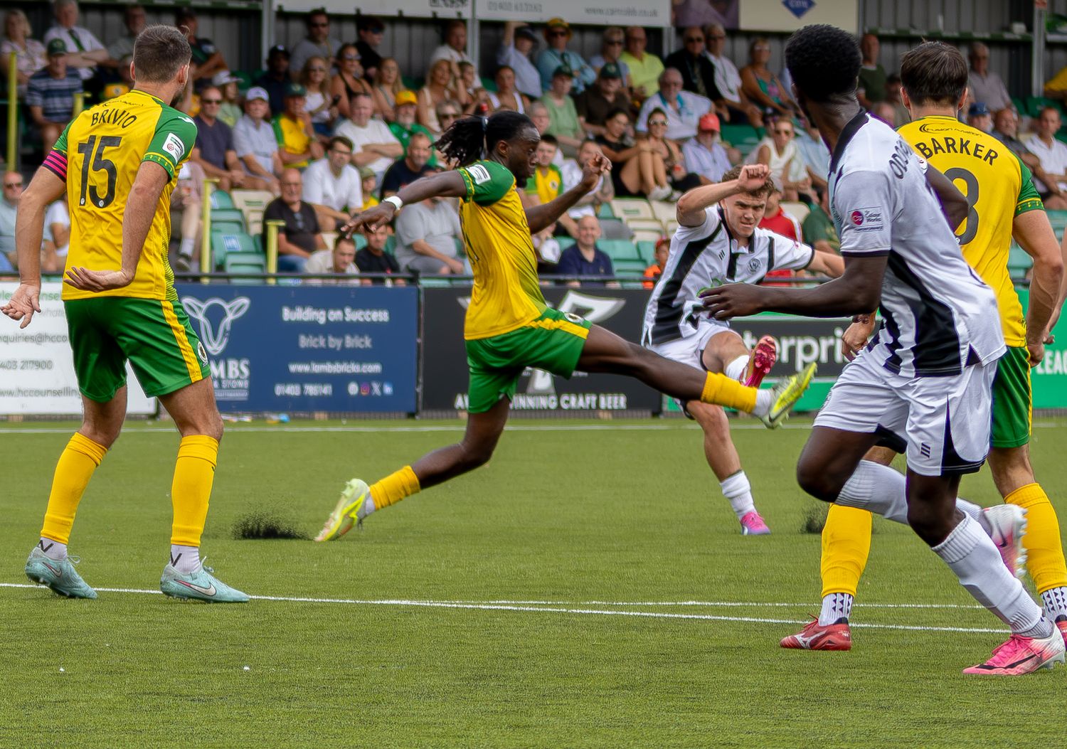 Players in yellow-green and black-white kits contest the ball in an intense outdoor football match.