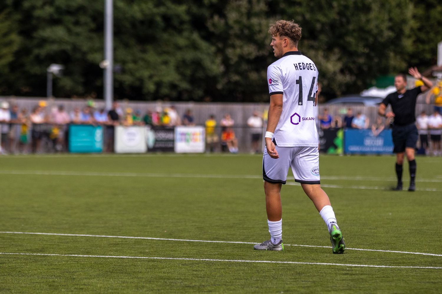 Football player number 14 in white kit looks back over shoulder on green pitch during match.