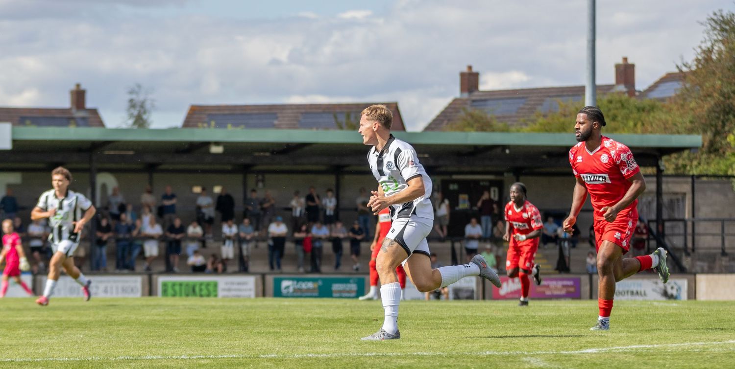 Female footballer in black and white kit sprints down the pitch during a competitive match.