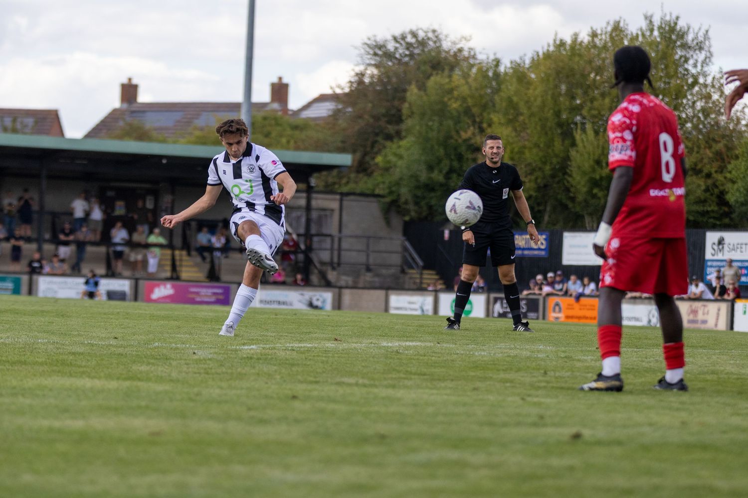 A player in black and white kit takes a powerful shot during a football match.