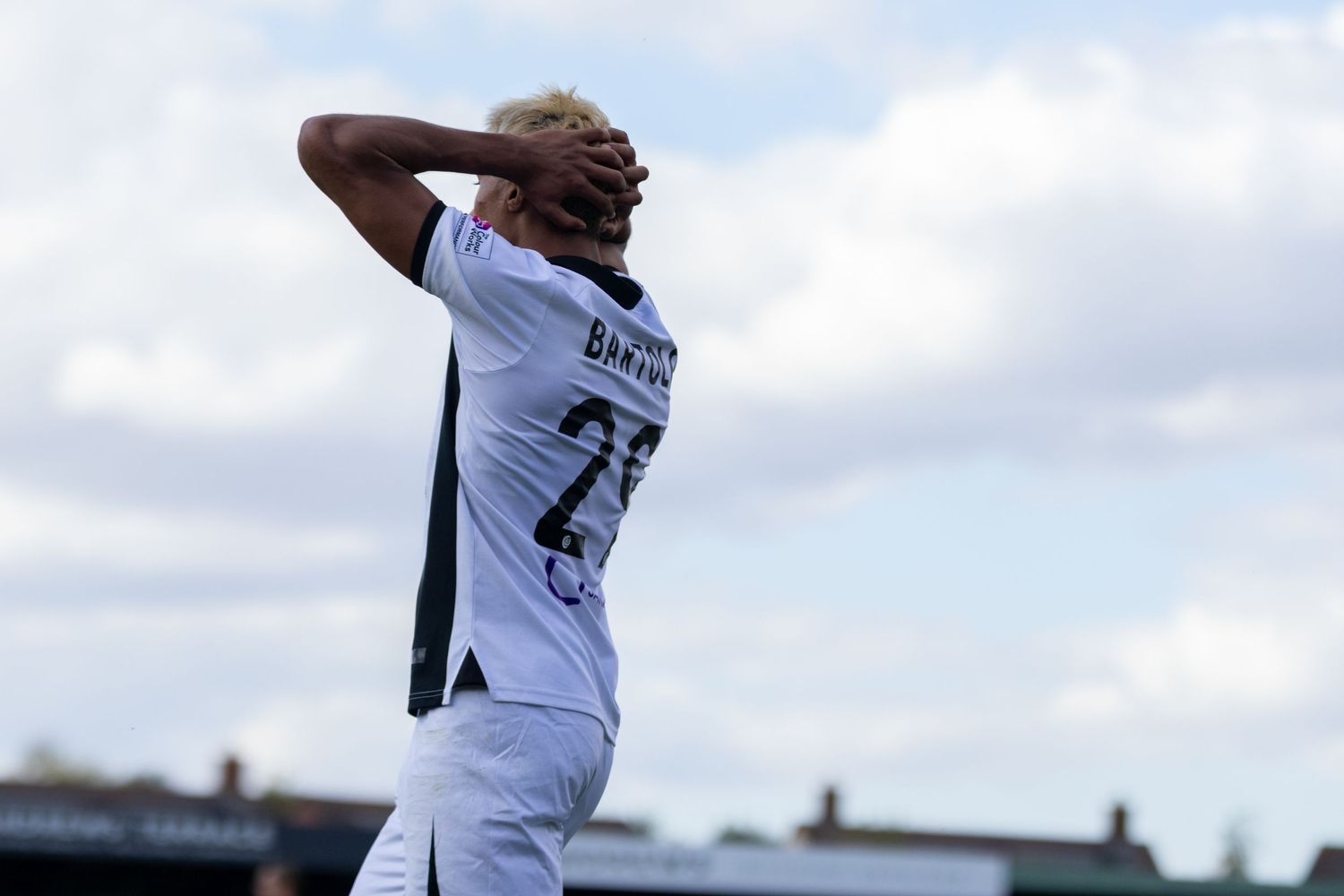 A frustrated footballer in white kit with number 22 holds his head in his hands during a match.