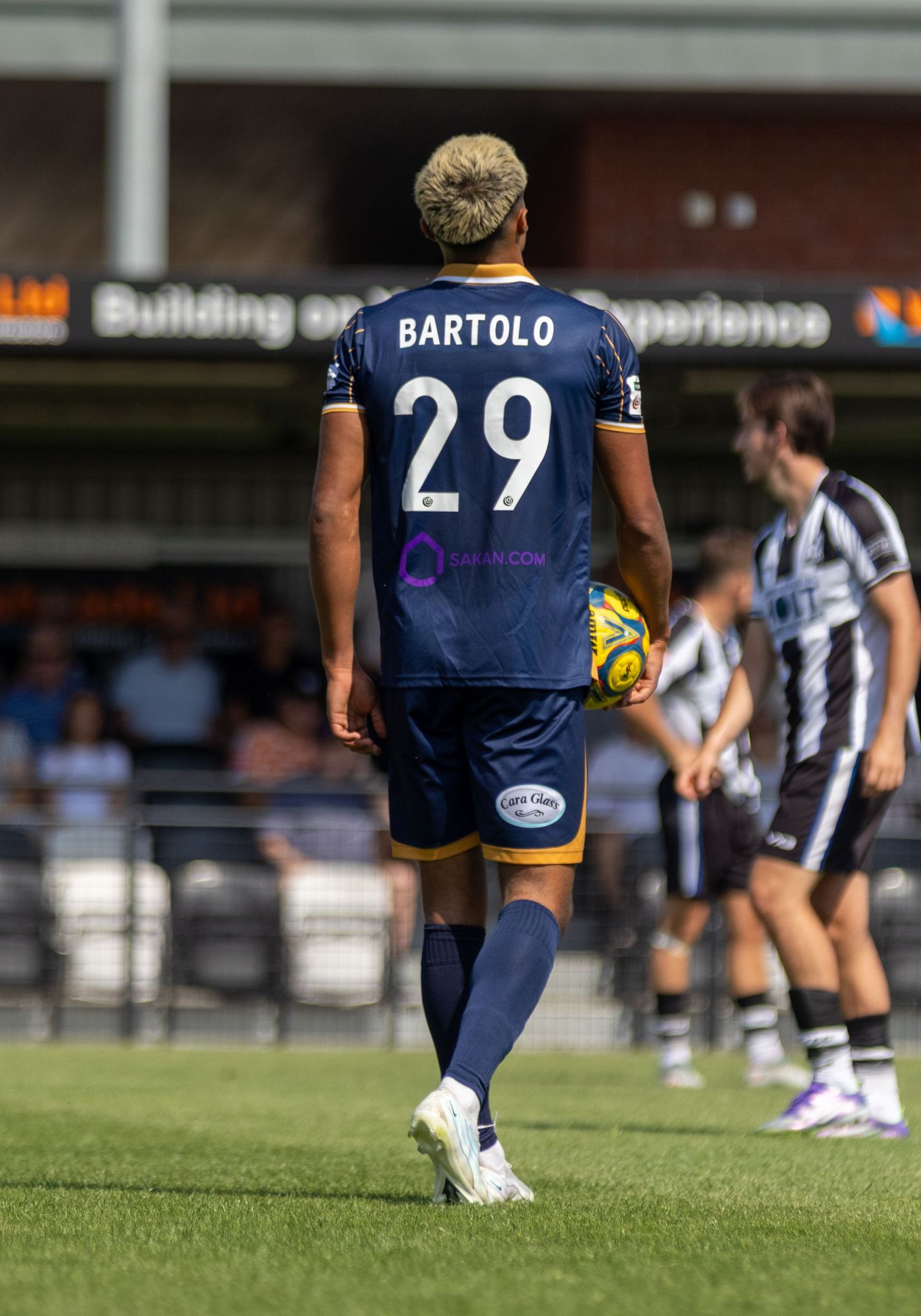 Footballer Bartolo wearing number 29 navy kit carrying ball onto pitch during game.