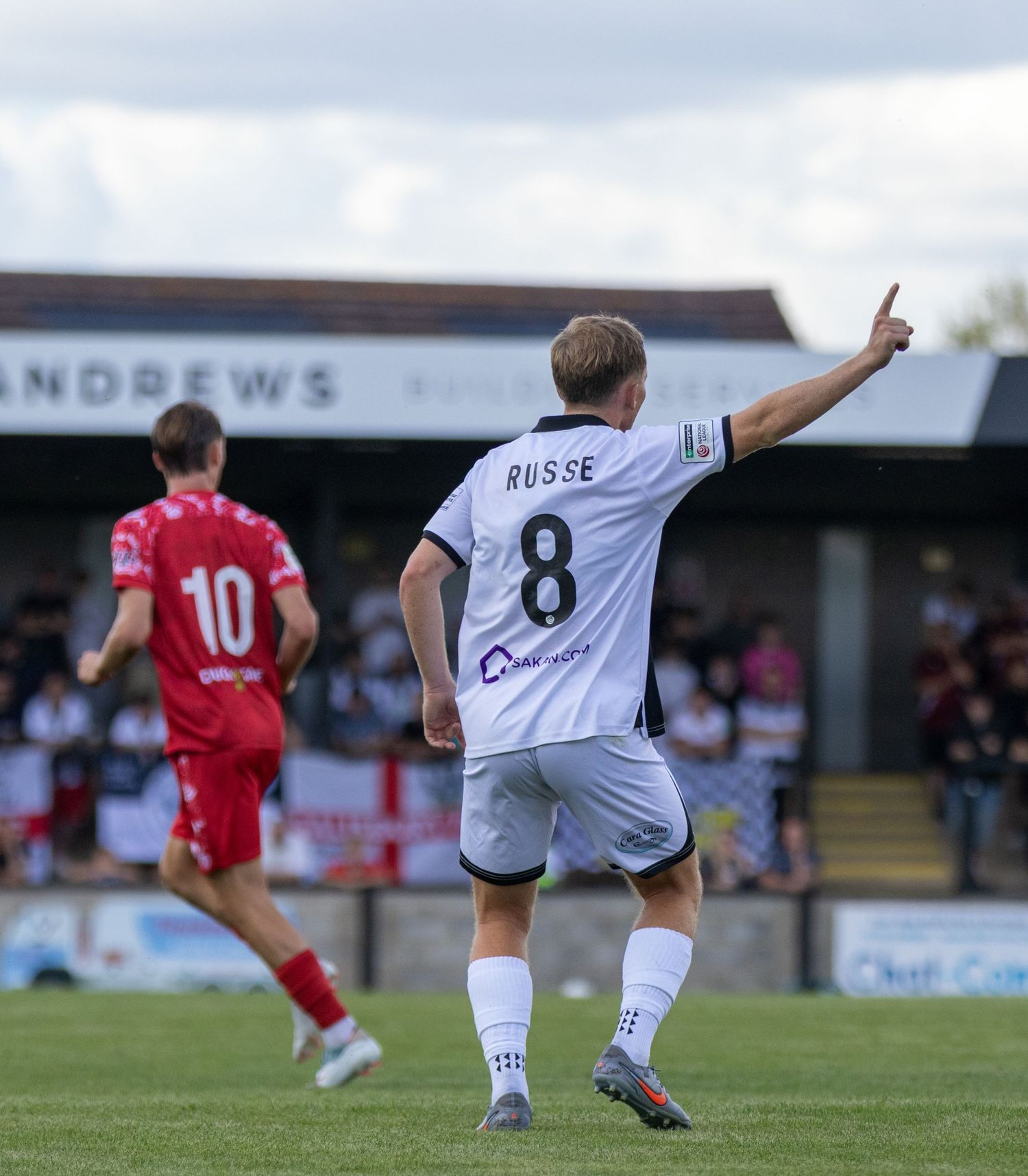 Player Russe wearing number 8 white jersey celebrates a goal pointing finger skyward during football match.