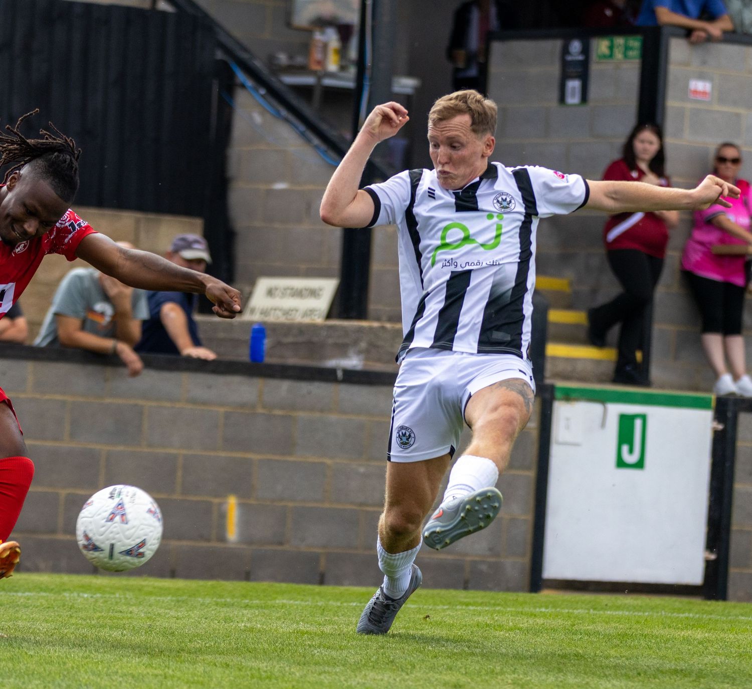 Soccer player in black and white kit kicks the ball during a competitive football match.